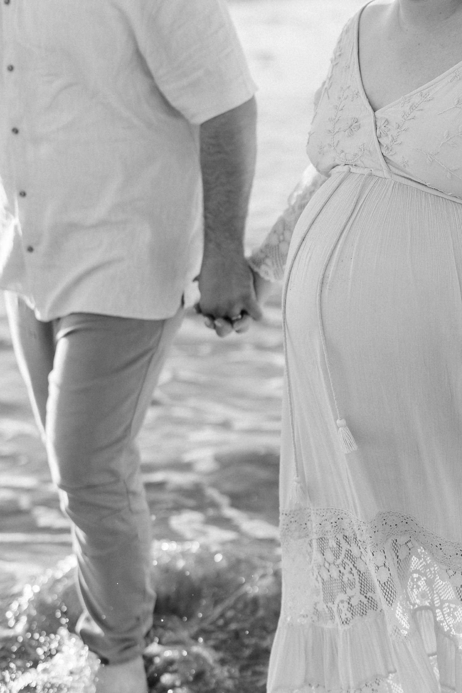 Detail shot of white lace maternity dress against beach scenery.