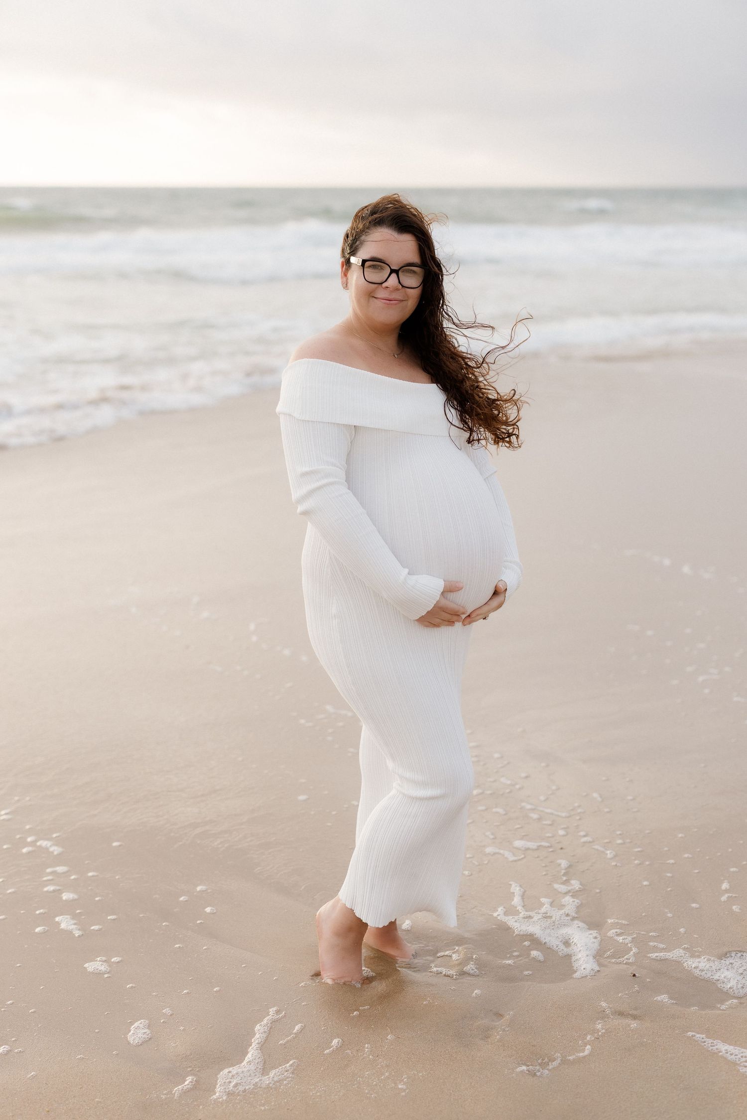 A person in a white dress twirls on the beach as waves roll in during golden hour.