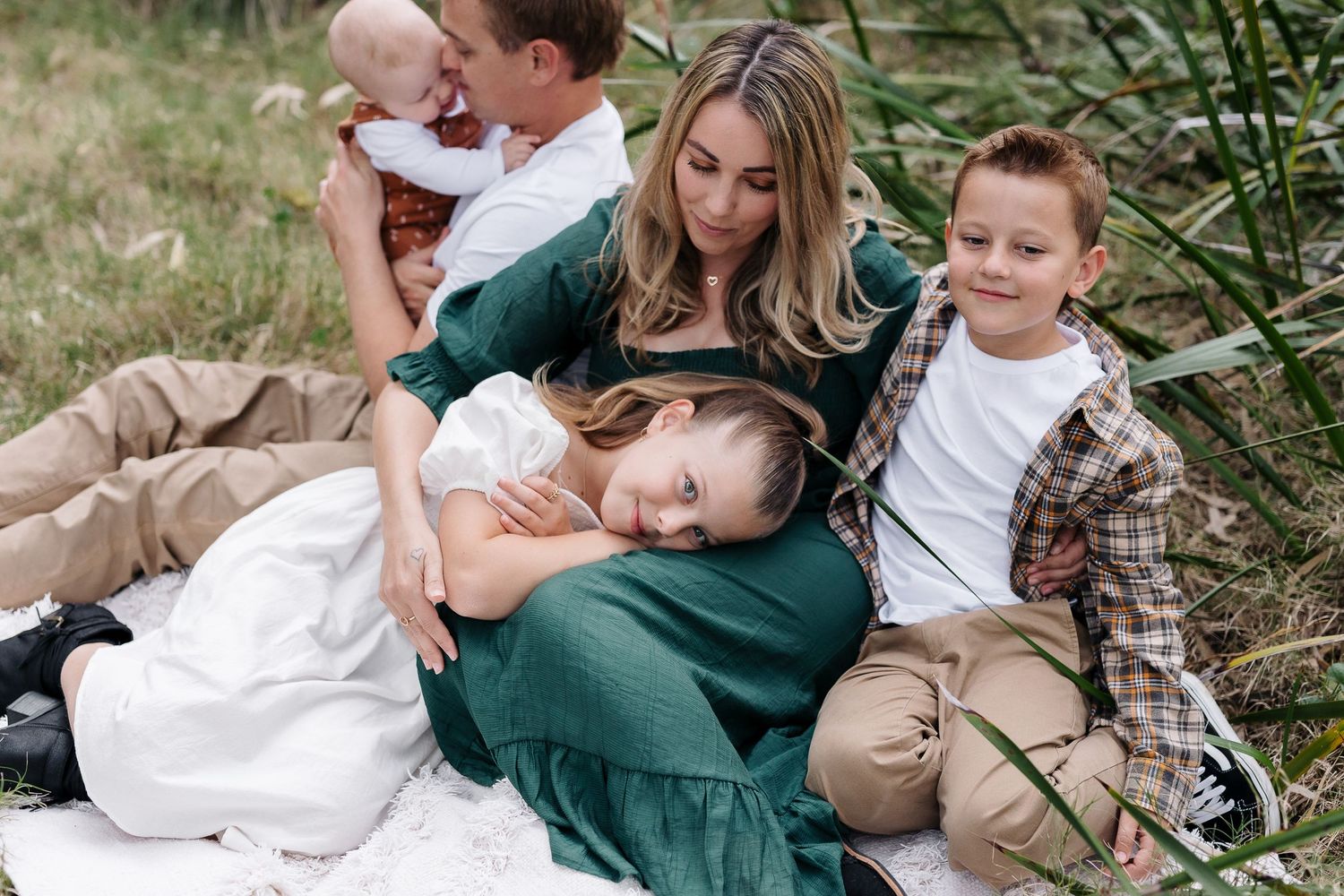 Intimate family photo session with everyone cuddled together on blanket outdoors.