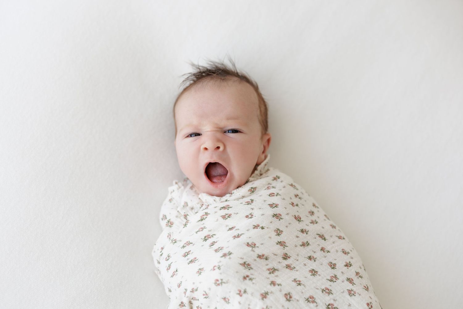 Swaddled baby lying on white background with big yawn.