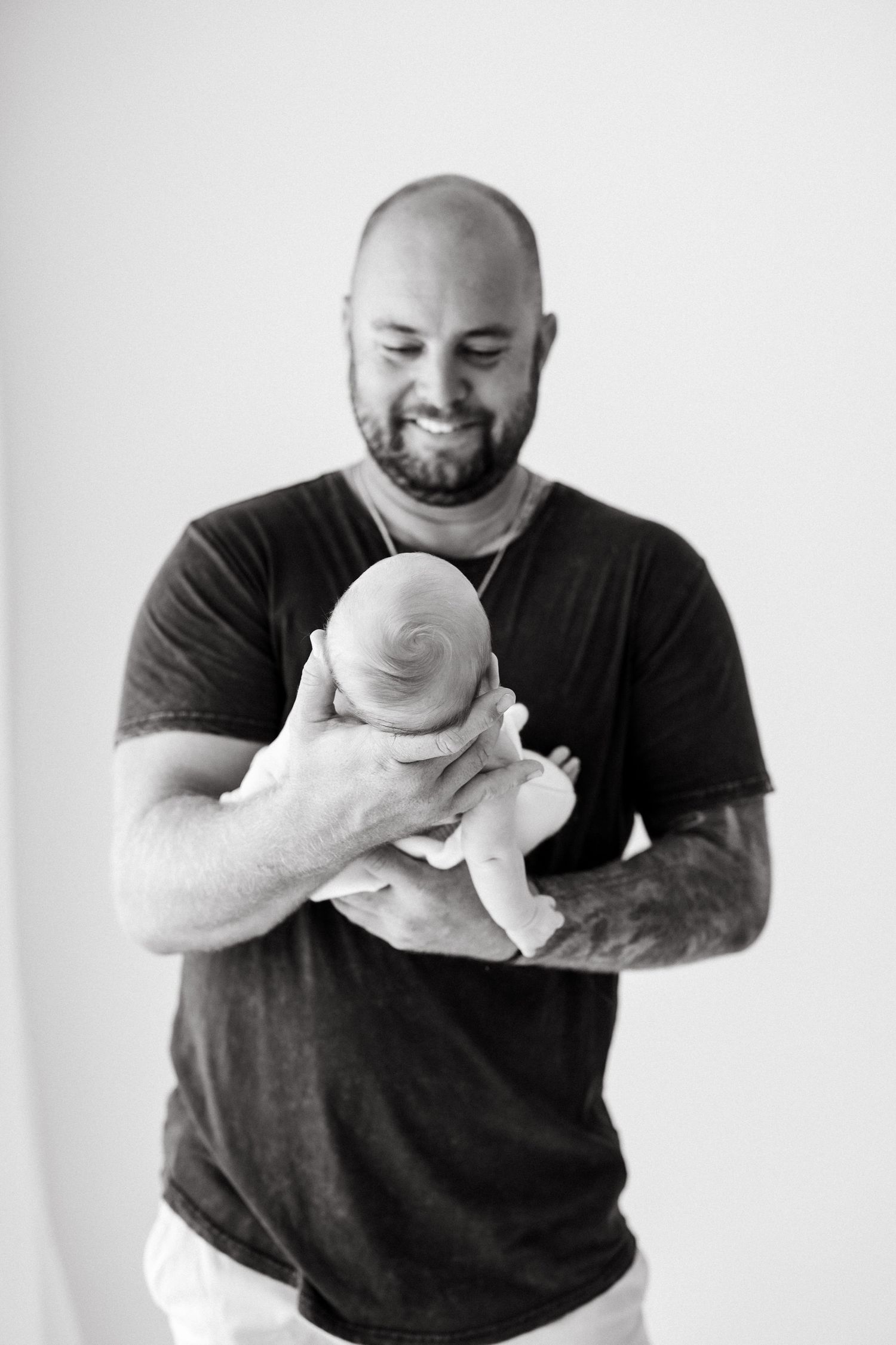 A heartwarming black and white photo of a bearded man in a dark t-shirt tenderly holding a newborn baby.