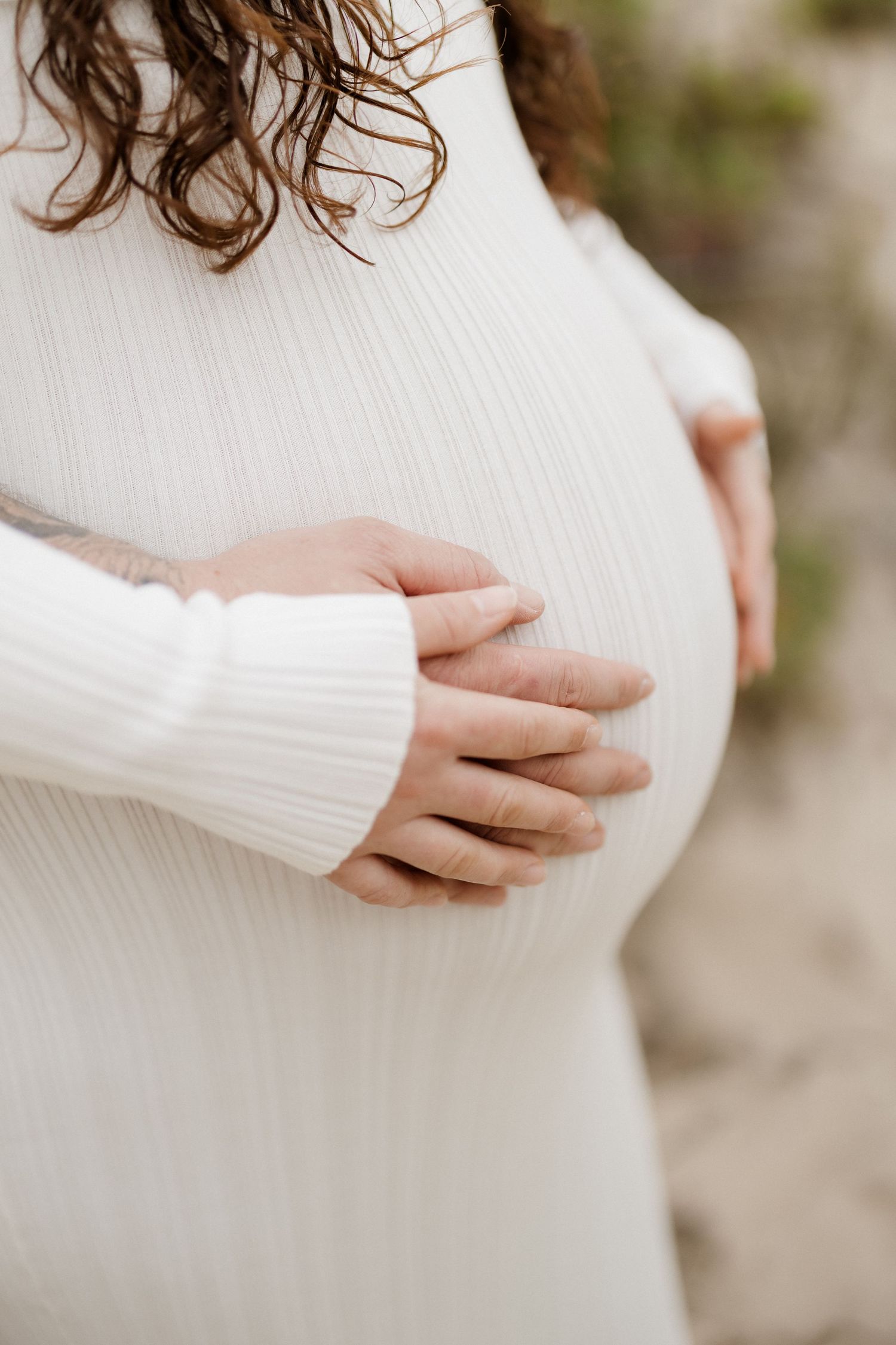 Close-up view of hands lovingly caressing a pregnant belly in a white sweater.