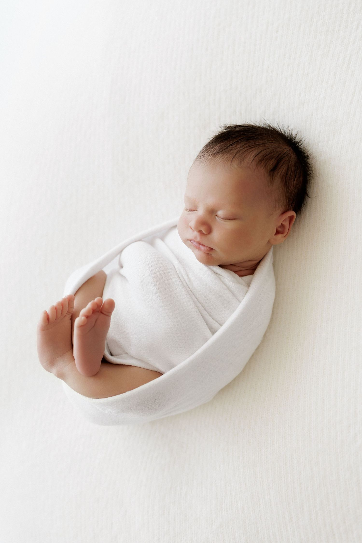 Sleeping newborn in white wrap on white background in minimalist style.