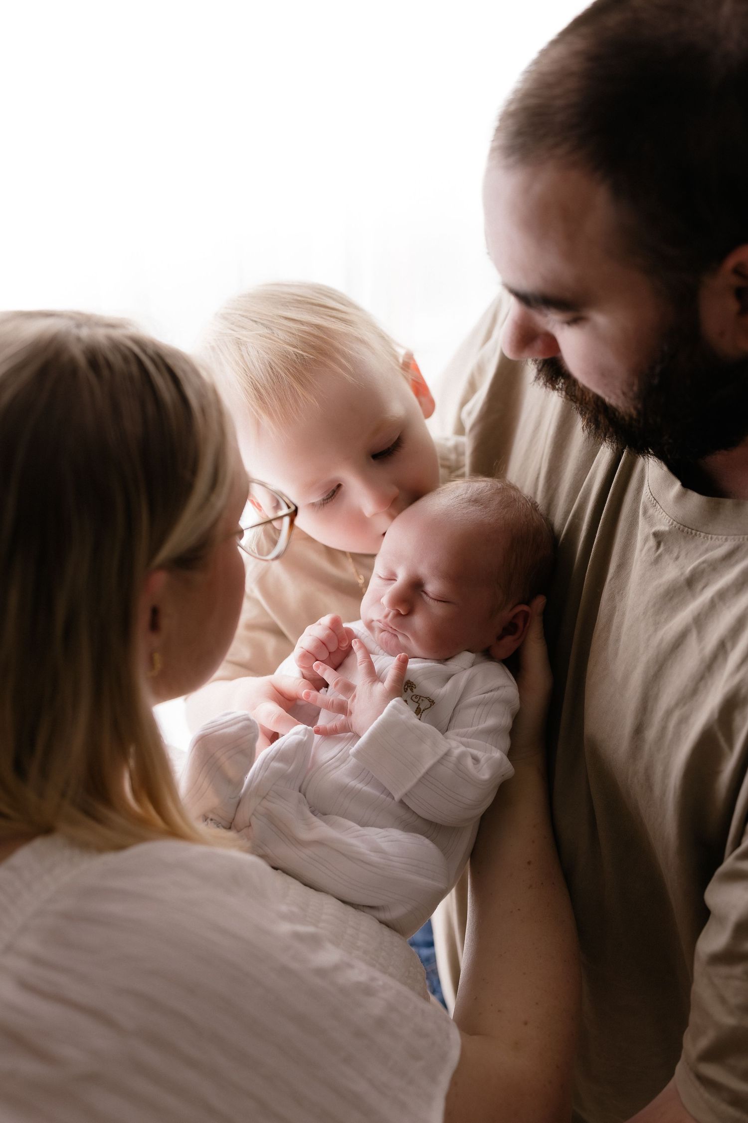 Family members sharing tender moments with a newborn baby in white clothing.