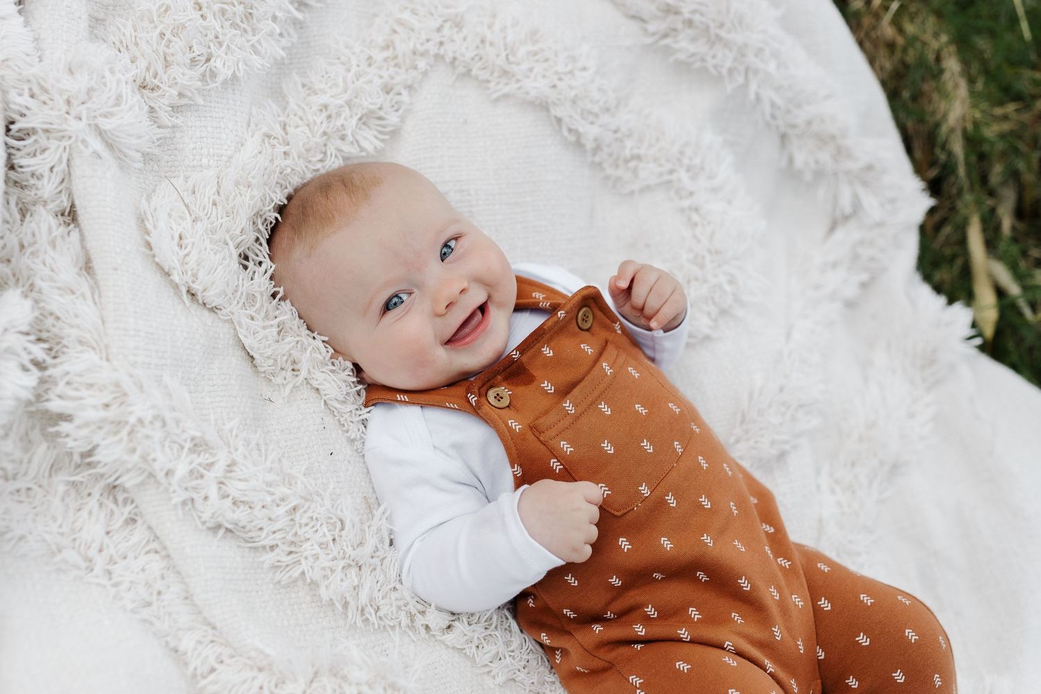 Cheerful baby in orange dotted overalls lying on white textured fabric.