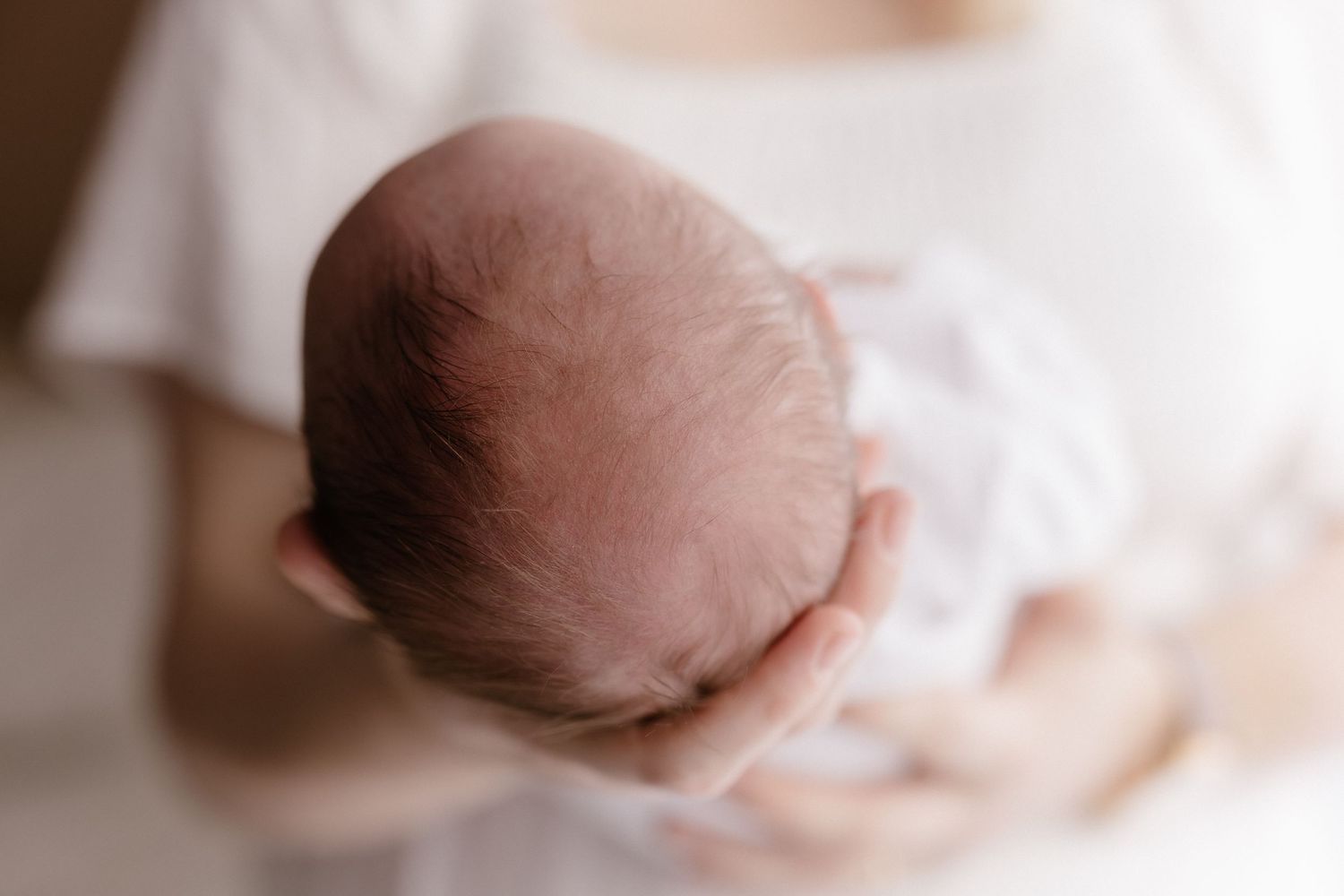Close-up of a newborn baby's head cradled gently in mother's arms in soft white wrap.