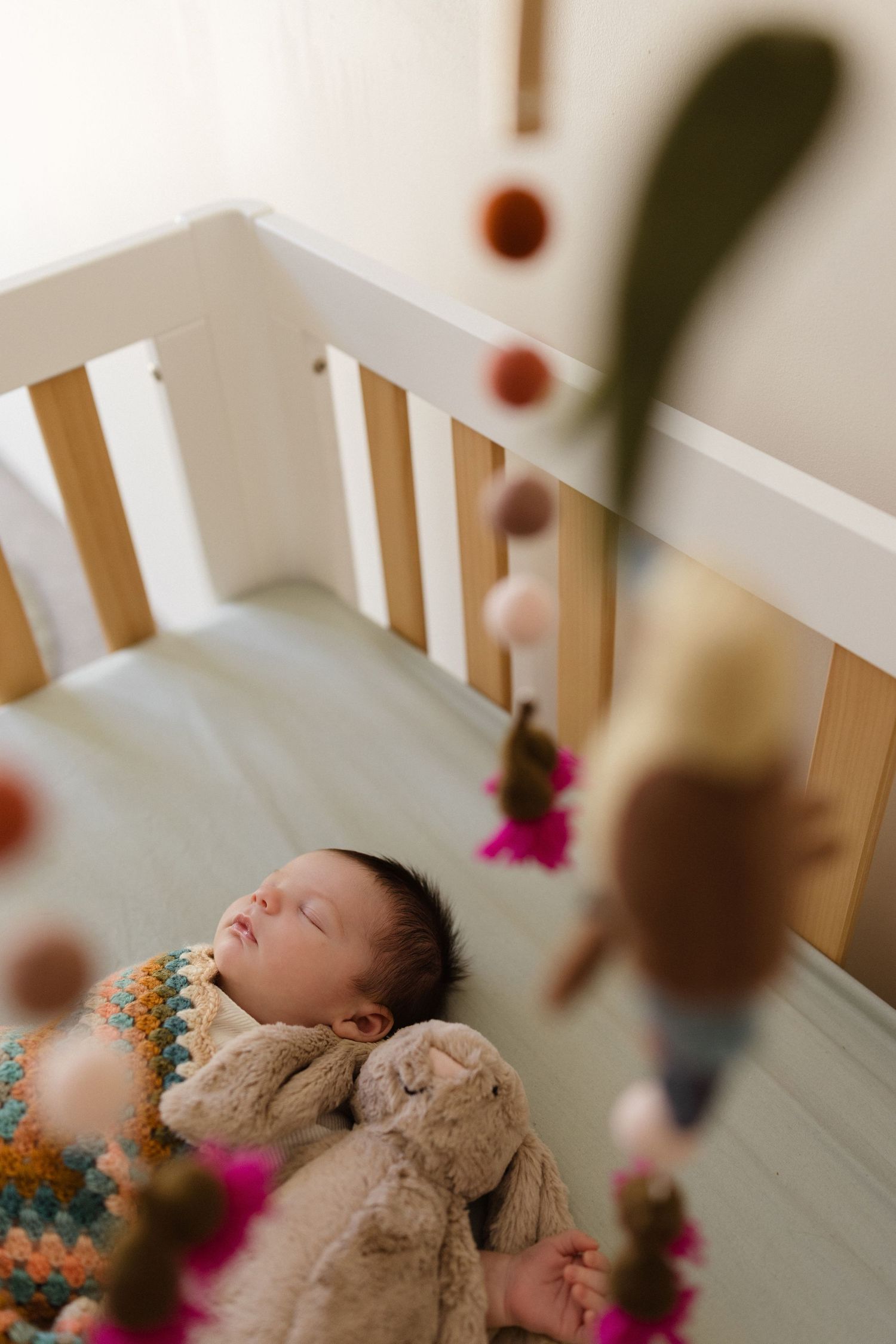 Sleeping baby in white crib with colorful blanket and decorative elements.