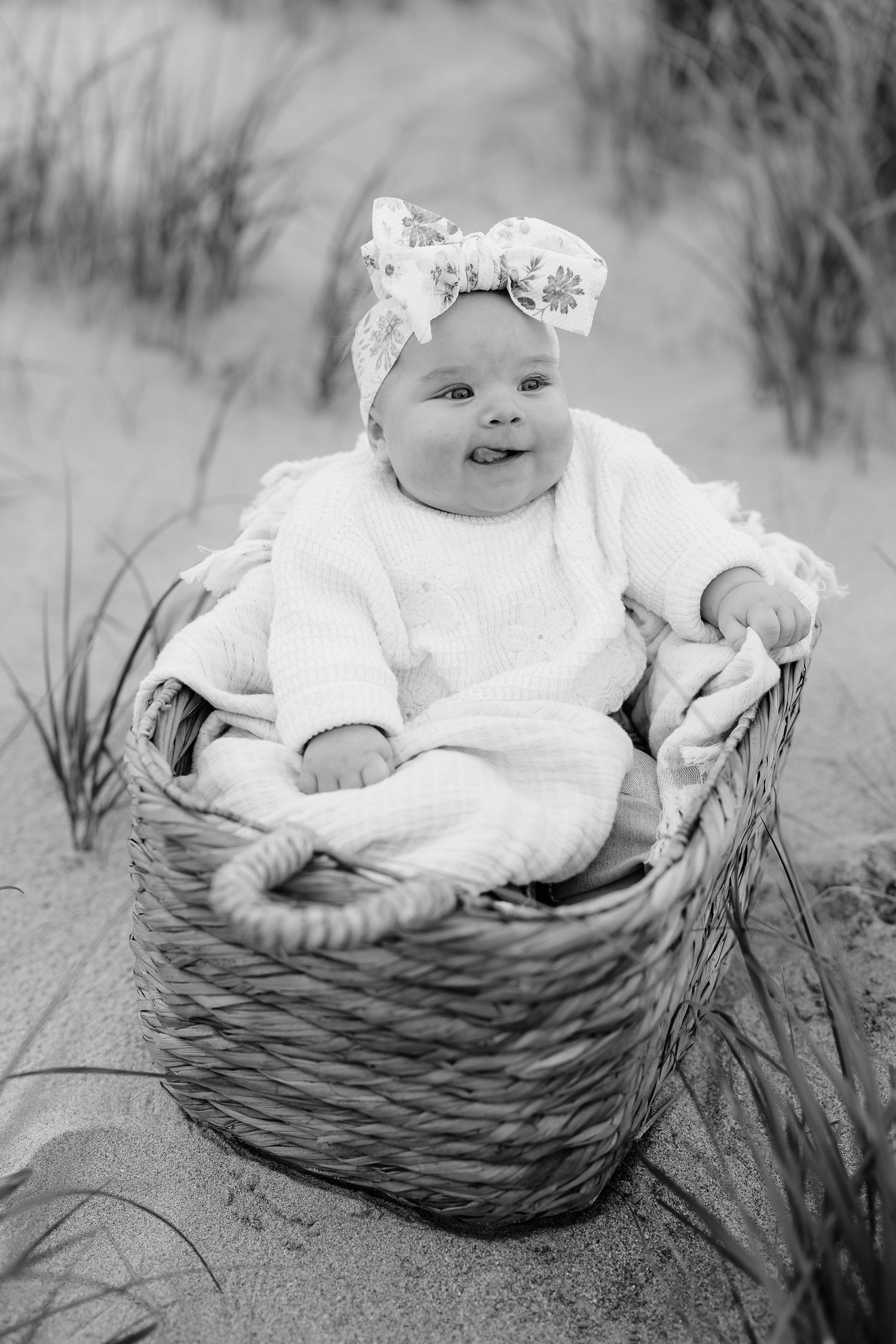 Baby sitting in woven basket on beach with happy expression.