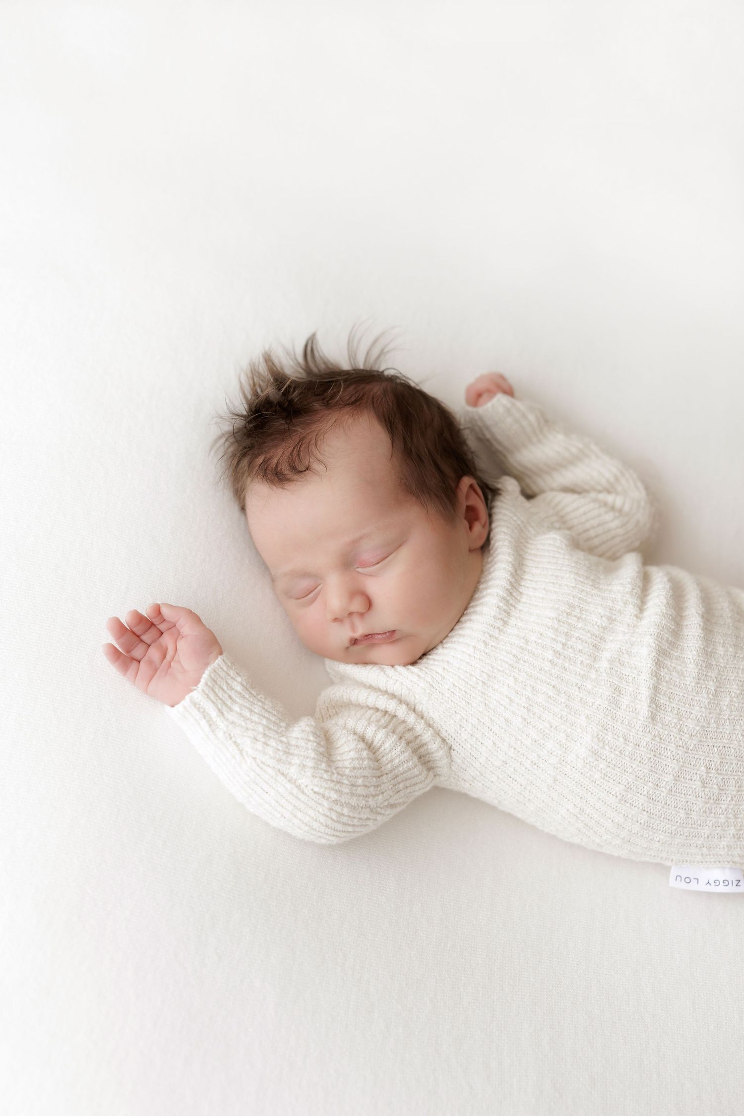 Peaceful sleeping newborn in white knit sweater on white background.