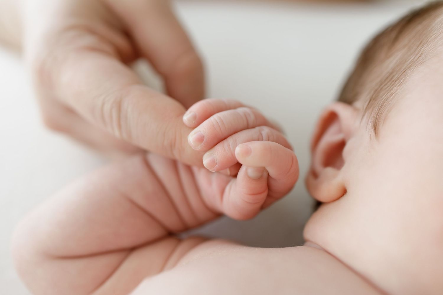 Close-up of baby's tiny hand and ear against soft white background.
