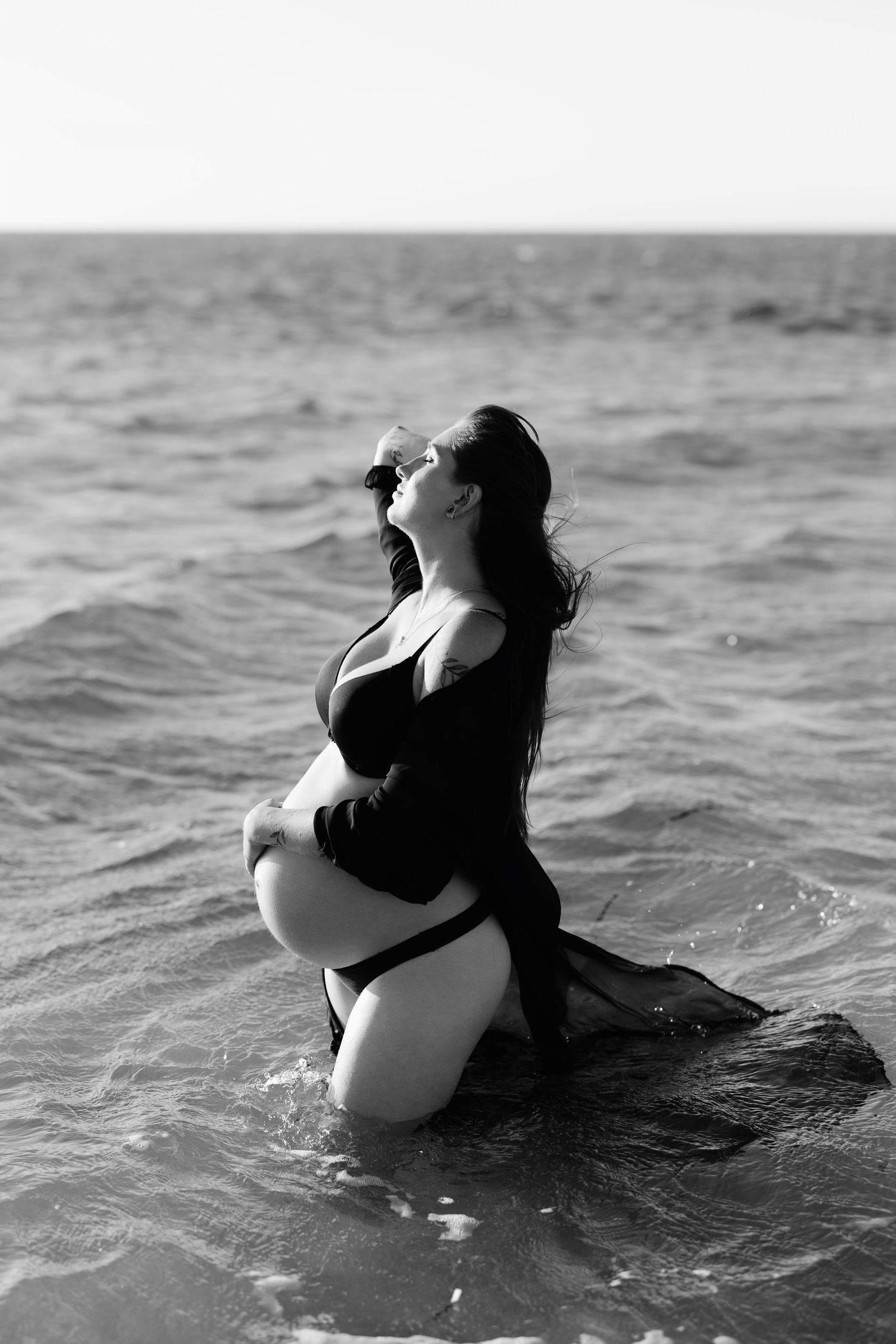 Black and white photos of a figure holding a baby in the ocean waves.
