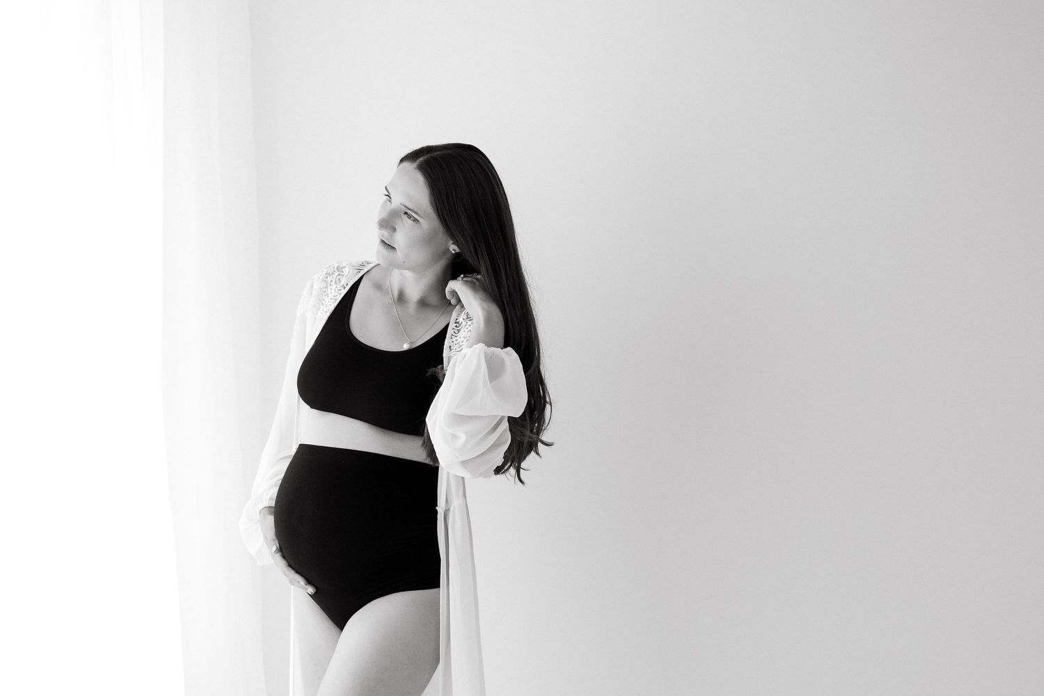 Black and white maternity portrait showing silhouette against minimalist white background.