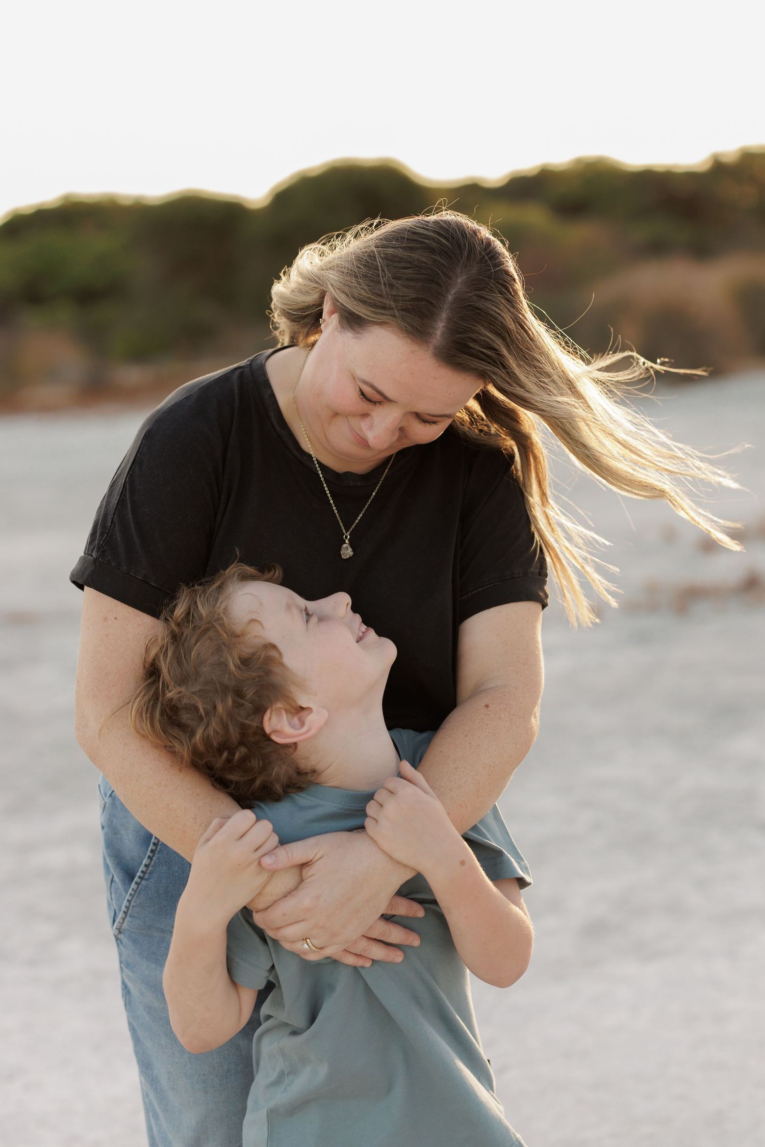 A tender embrace between two people sharing a playful moment on the beach at sunset.