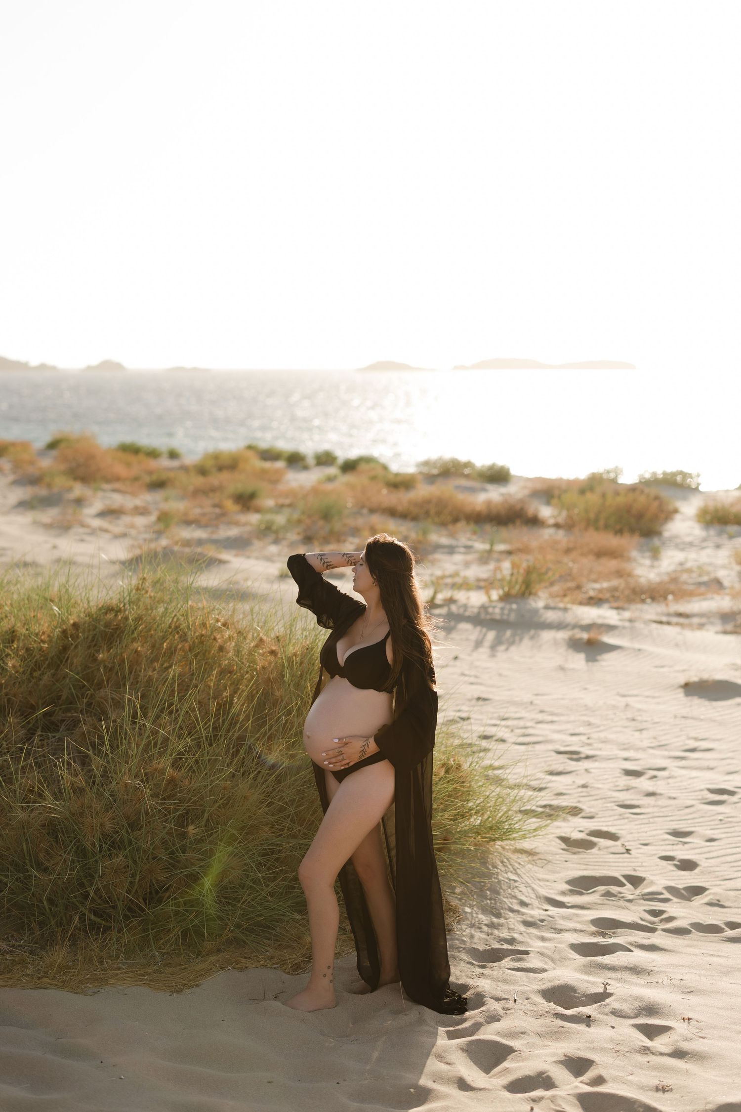 Maternity photoshoot at sunset on sandy beach with flowing black dress.