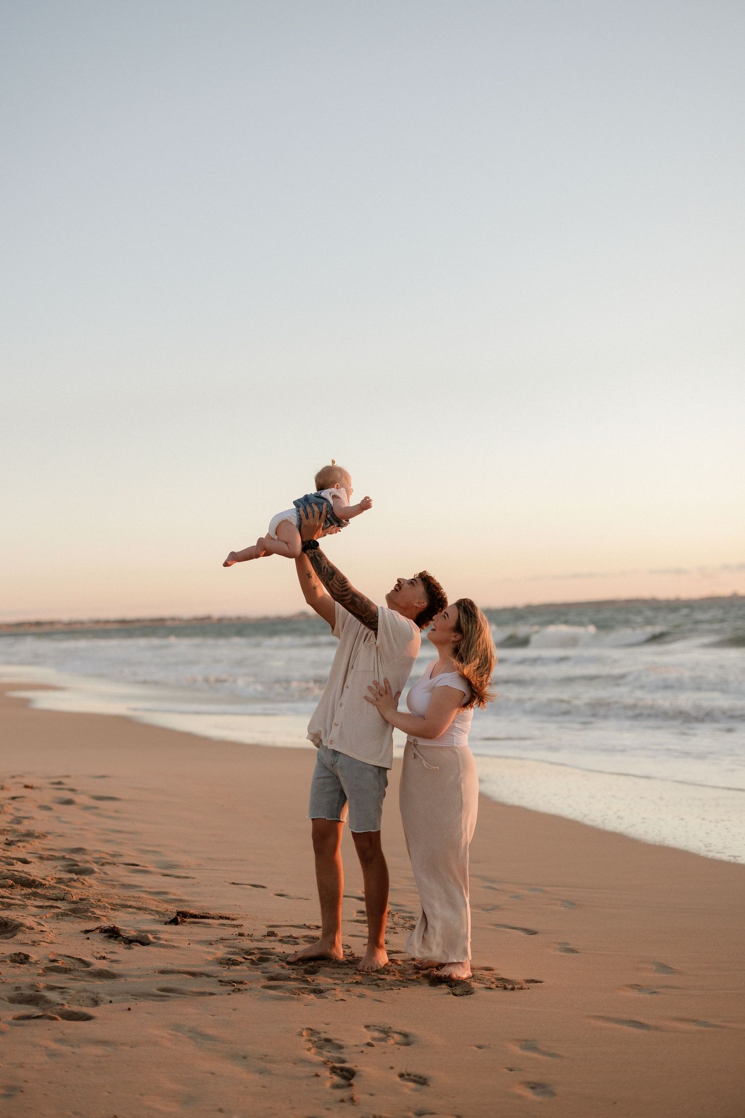 Family playing and laughing together on a sandy beach at sunset.