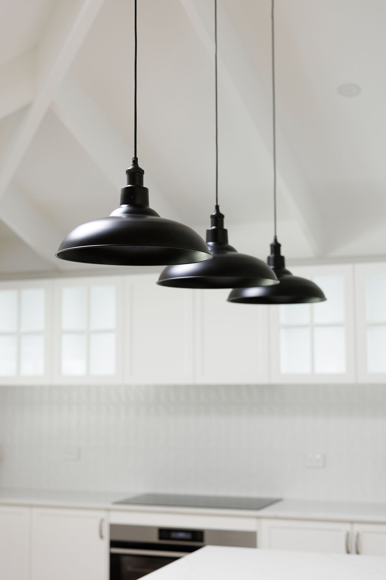 Modern white kitchen interior with black pendant lights hanging over counter and white cabinets in minimalist style.