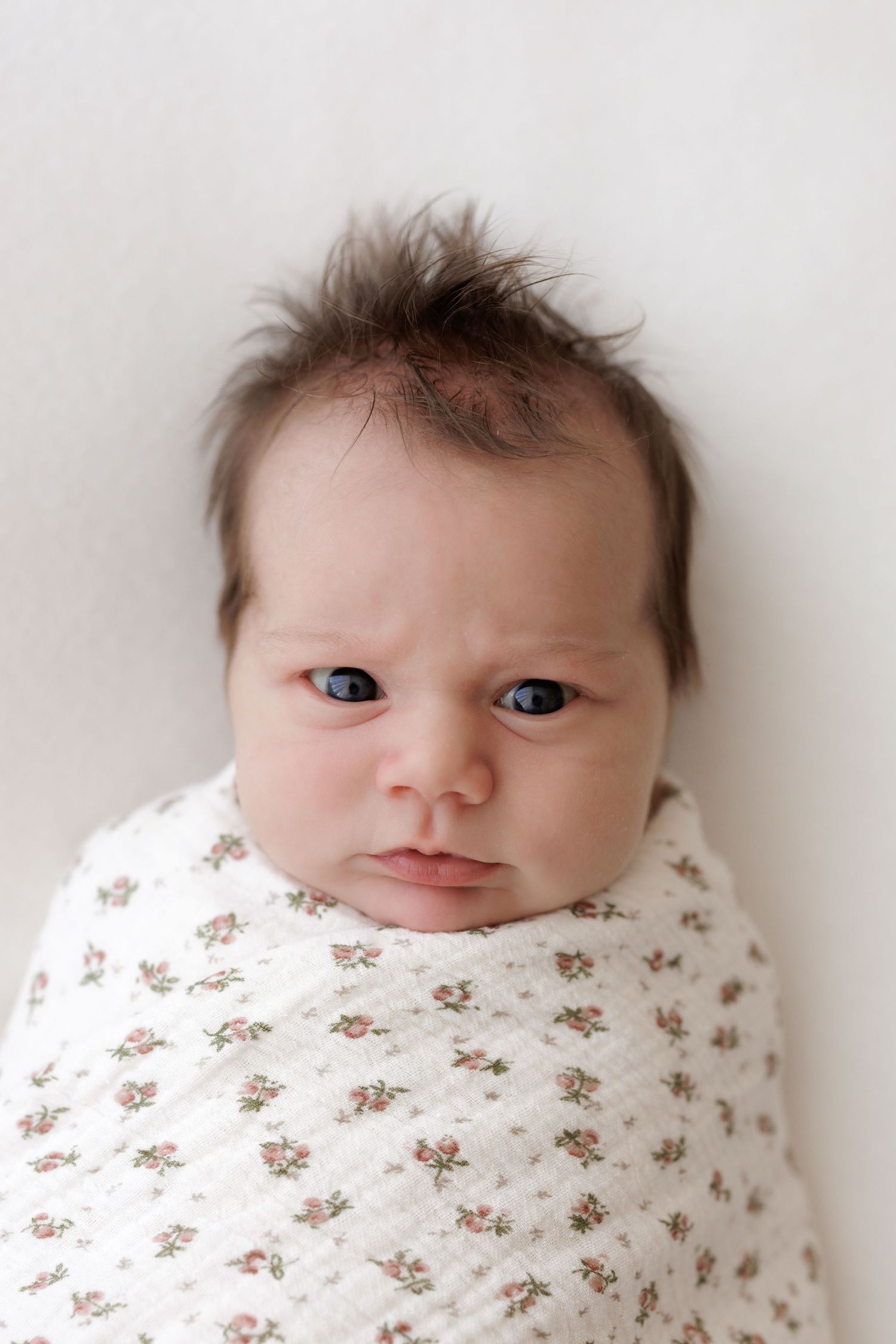 Newborn wrapped in floral swaddle blanket on white background.