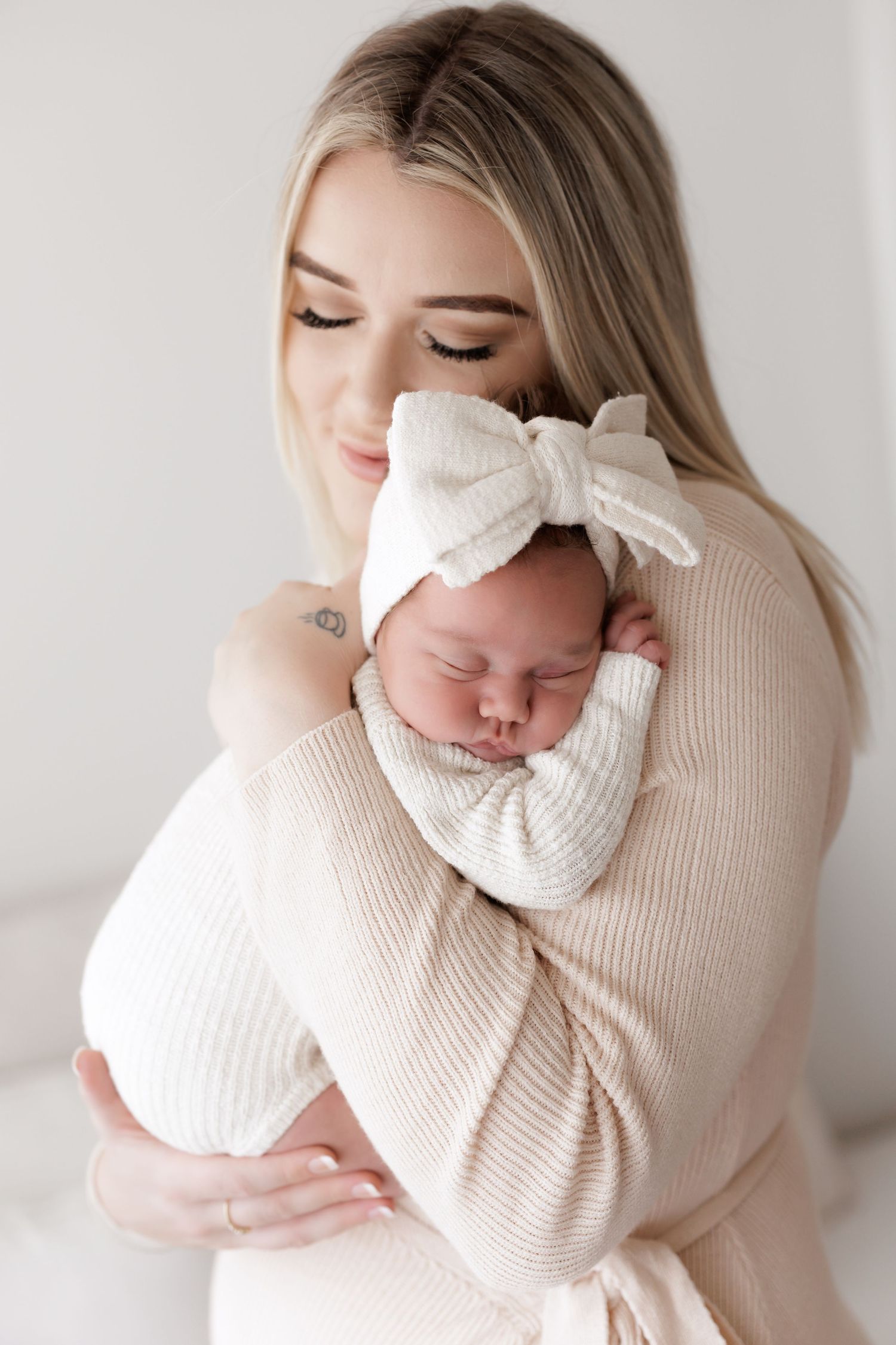 Intimate portrait of parent cradling sleeping newborn in cream colored knitwear.