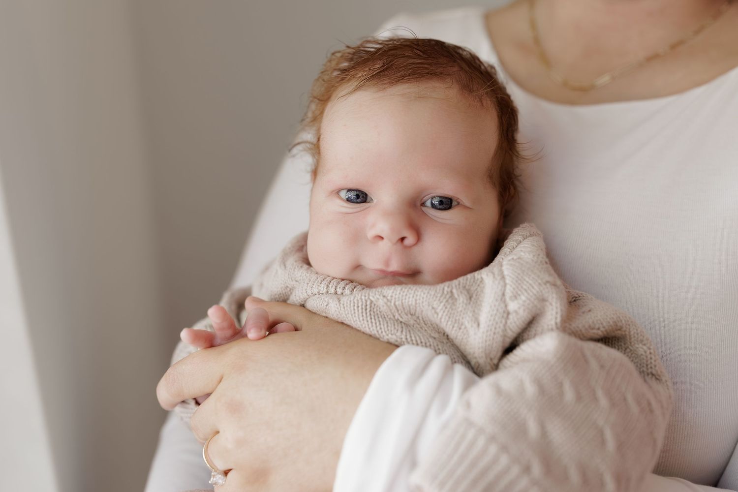 A newborn baby with blue eyes wrapped in a soft blanket being cradled in a mother's arms.