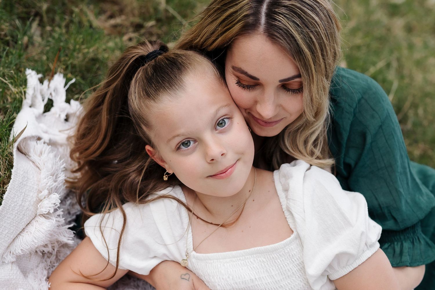 Tender moment shared outdoors on white blanket with natural background.