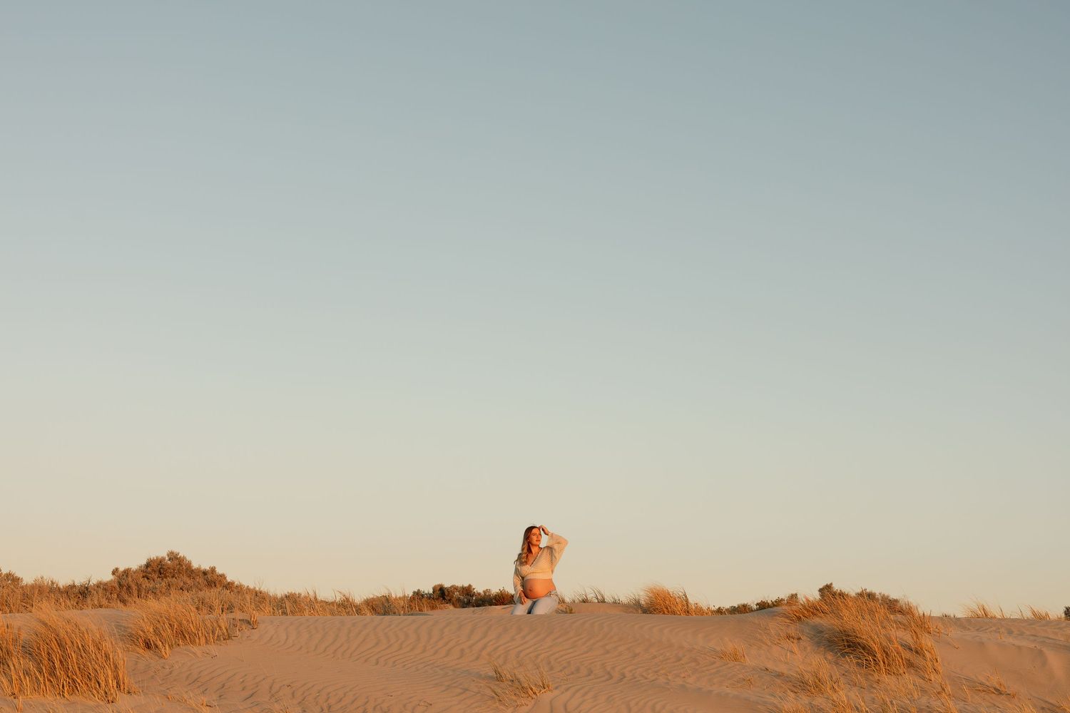 Silhouette figure sitting alone on sand dune during golden sunset.