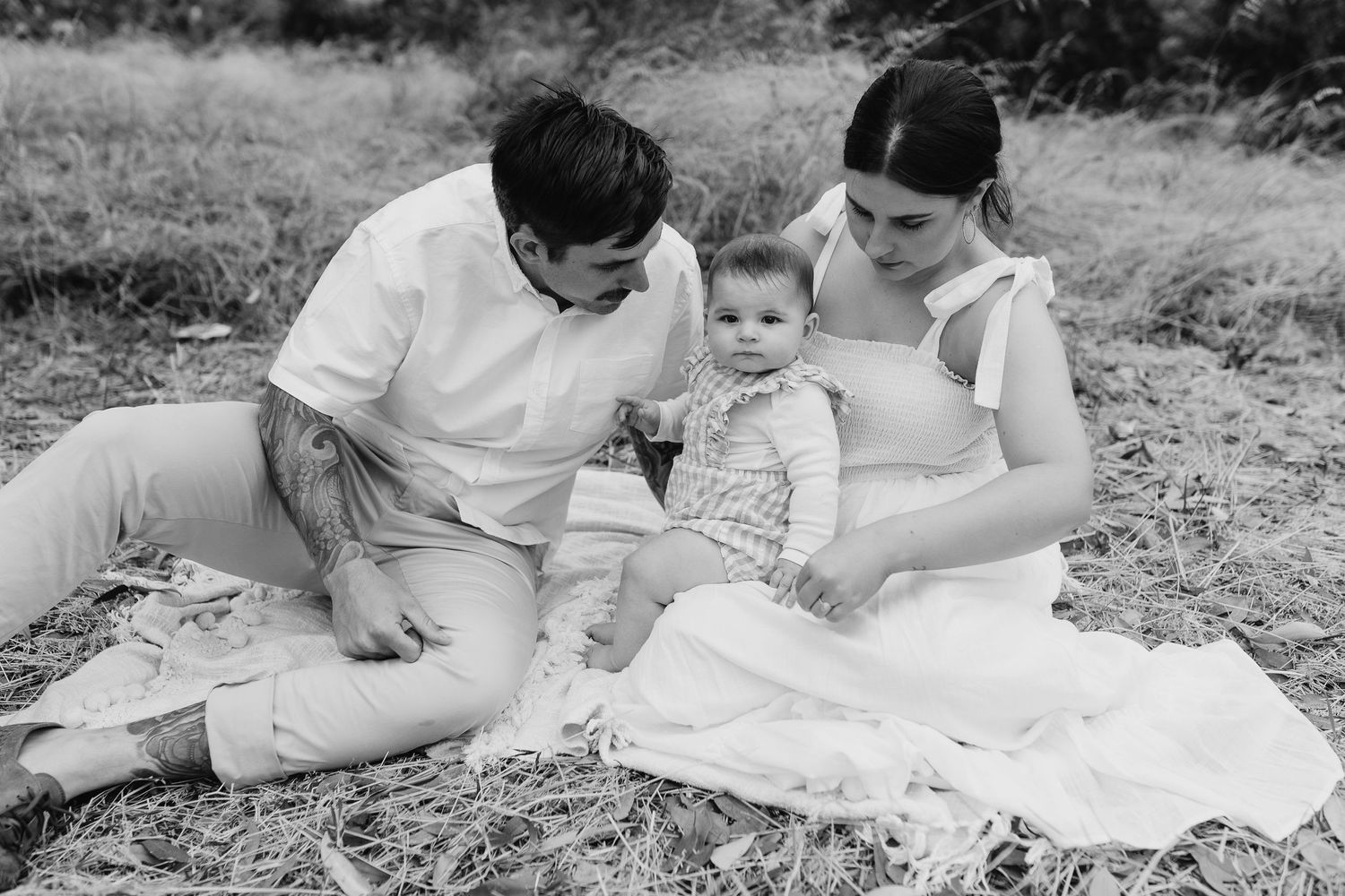 Black and white photo of family sitting together on blanket outdoors.