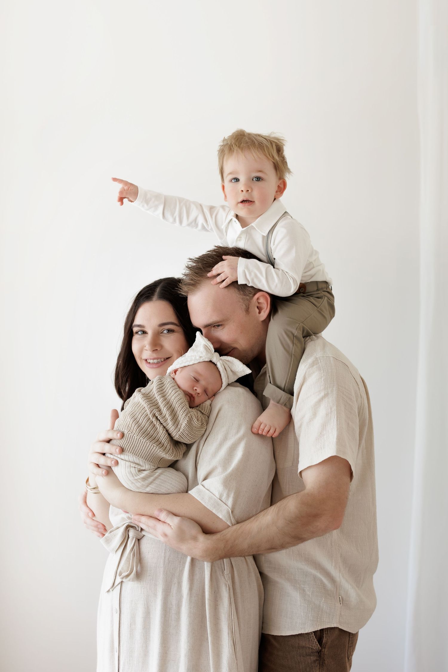 Family of four poses together against white wall in neutral clothing.