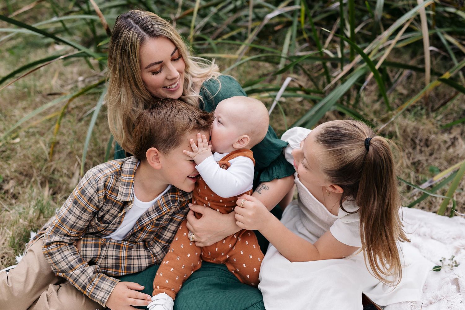 A joyful family moment shared on a white blanket outdoors amongst tall grasses.