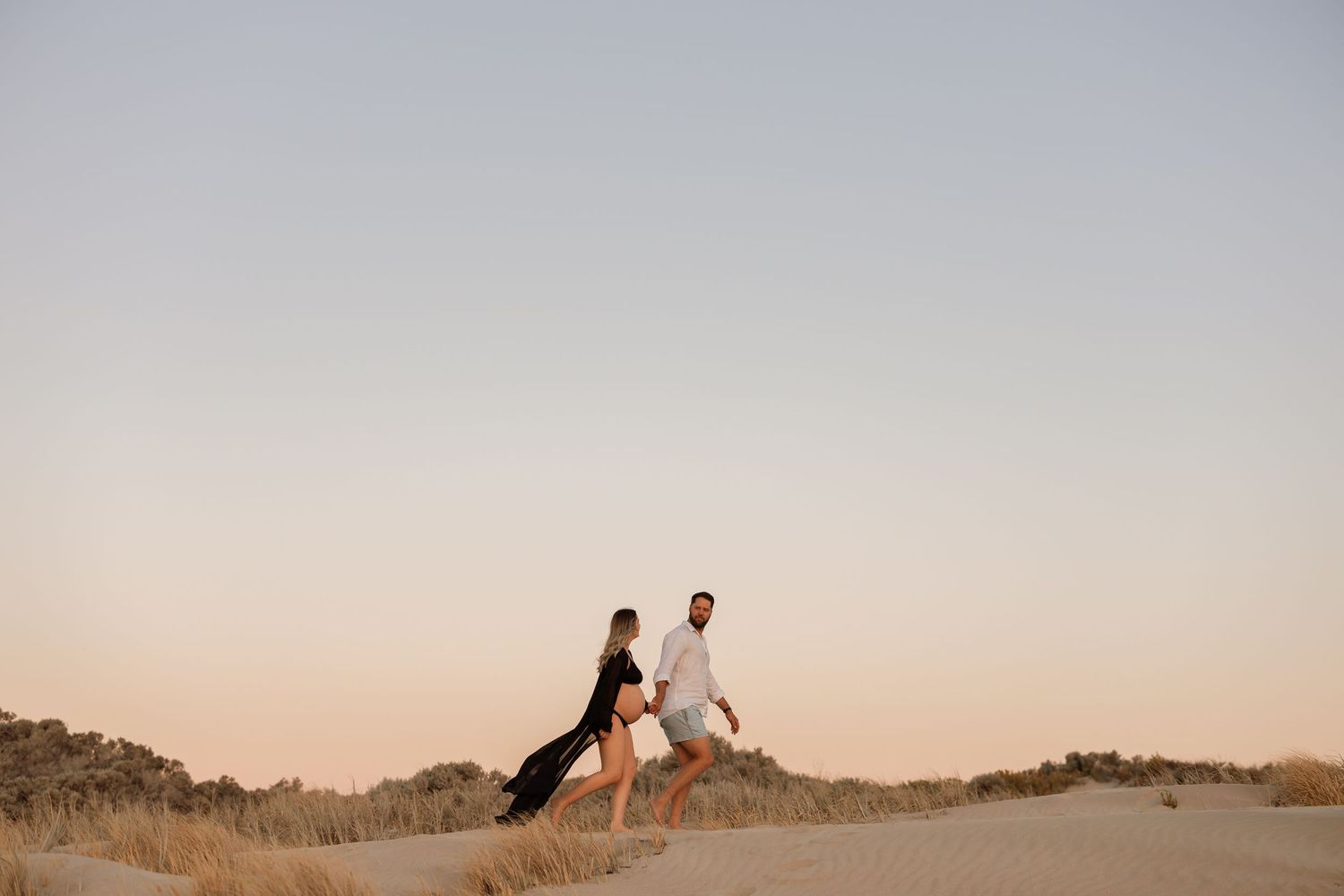 Two figures walking together along coastal dunes at dusk.