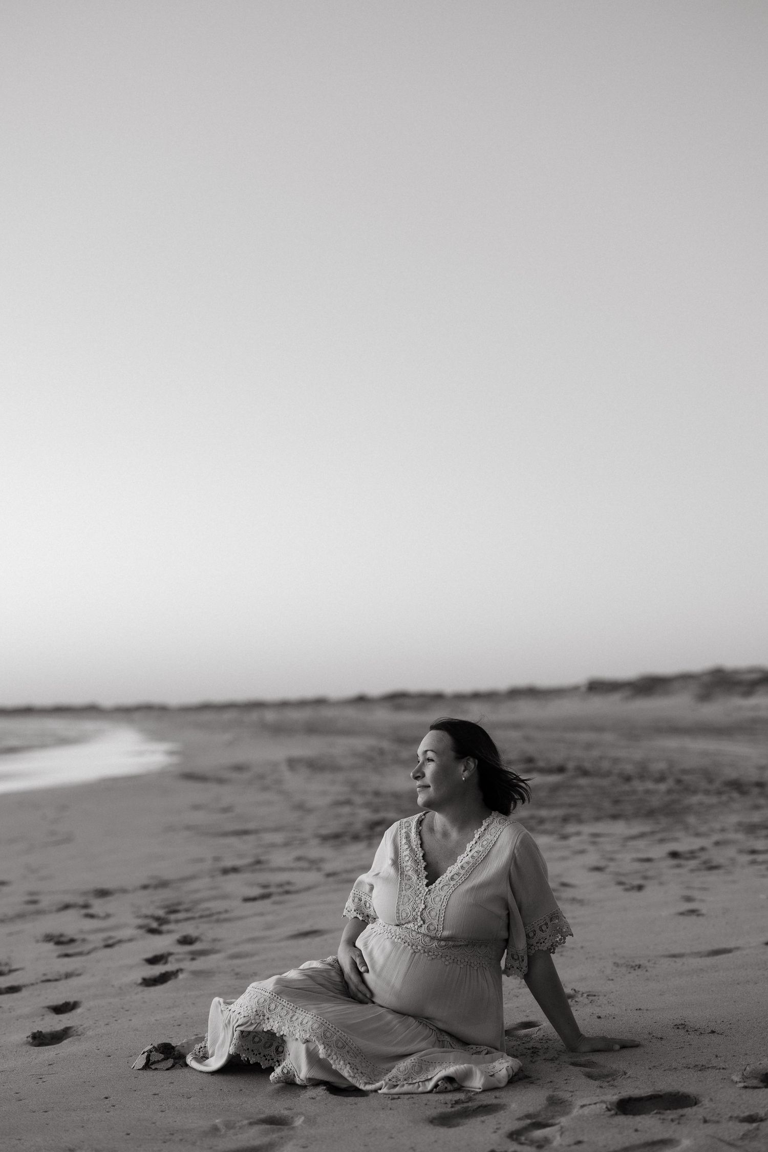 Woman in a white dress lying gracefully on a sandy beach at sunset.