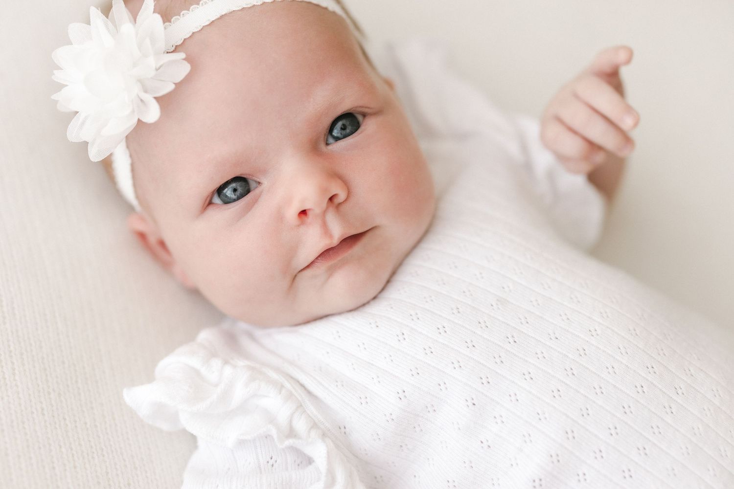 Close up of baby wearing white outfit and floral headband on light background.