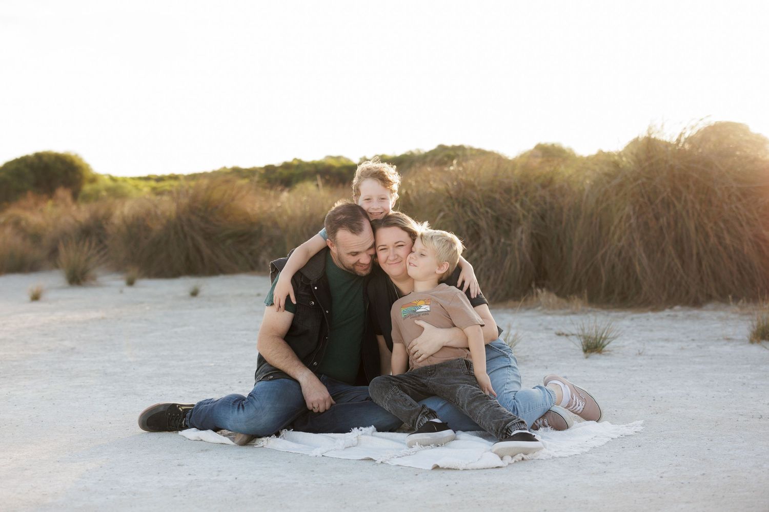 Family group sitting together on sandy beach at sunset.