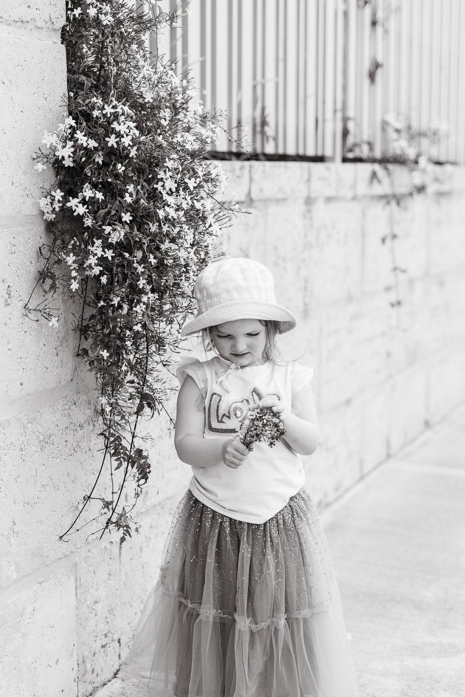 Black and white portrait against a wall with delicate climbing flowers and a bucket hat.
