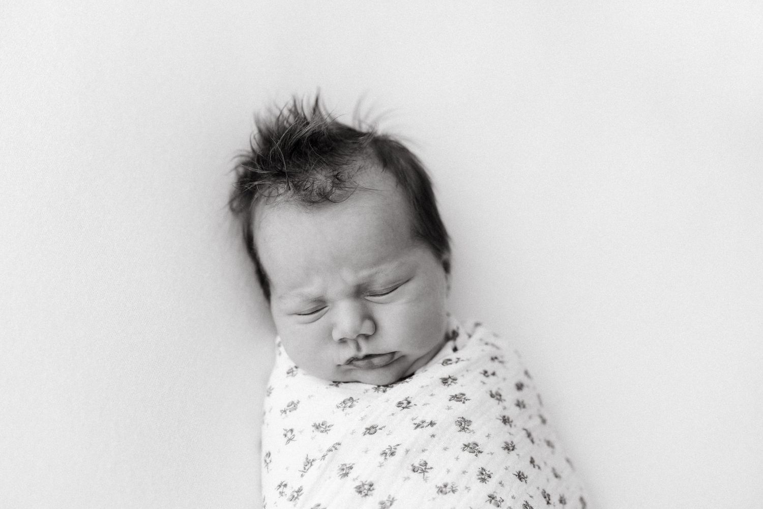 Peaceful sleeping newborn wrapped in floral swaddle against white background.