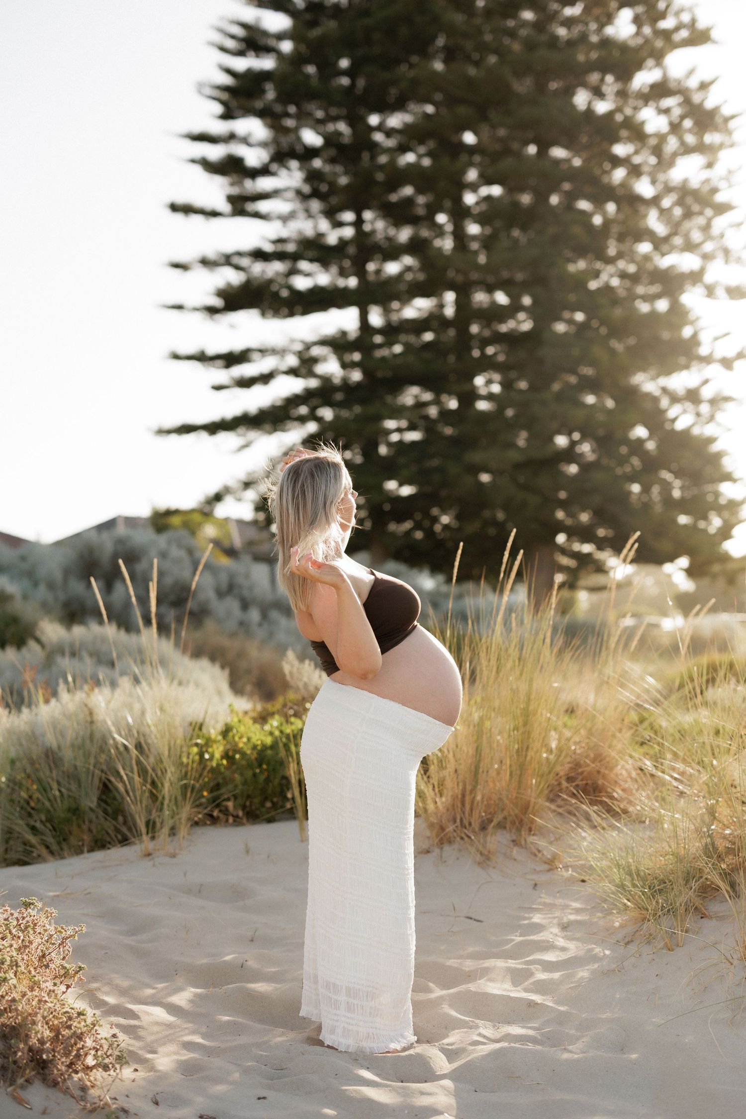 Woman in white dress standing among beach grass during golden hour.
