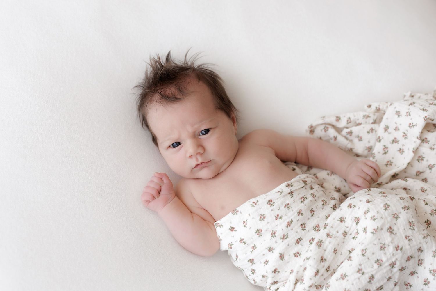 Baby partially covered with floral print blanket on white background.