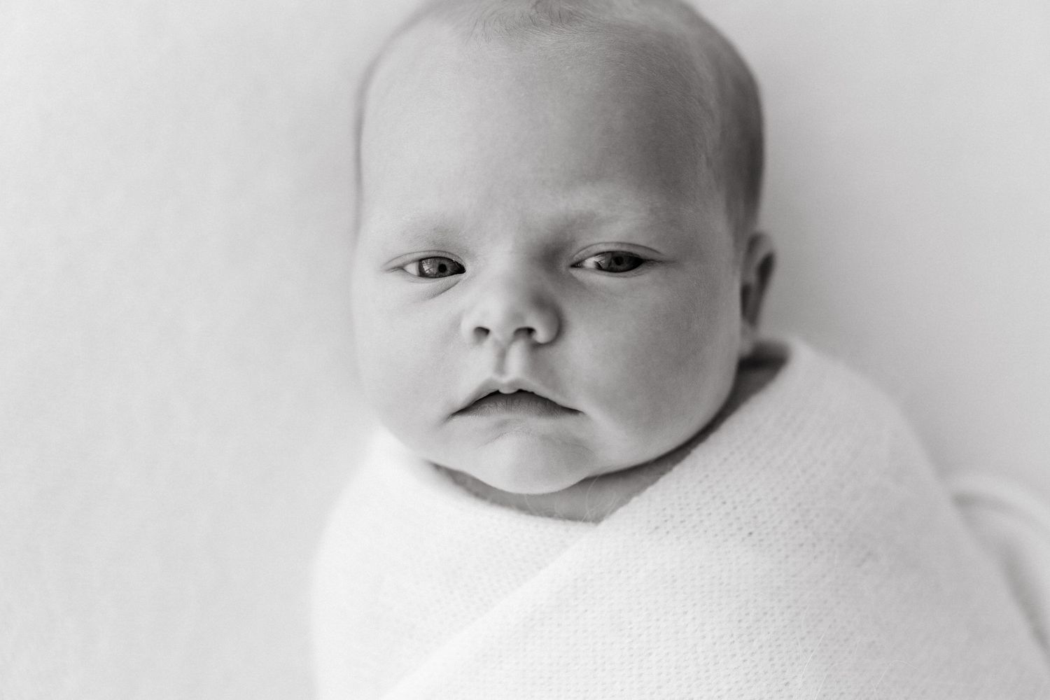 Black and white close-up portrait of swaddled infant.