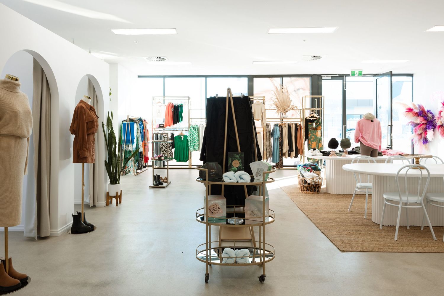 Interior view of a modern retail clothing store with white walls, wooden floors and racks of fashion merchandise.