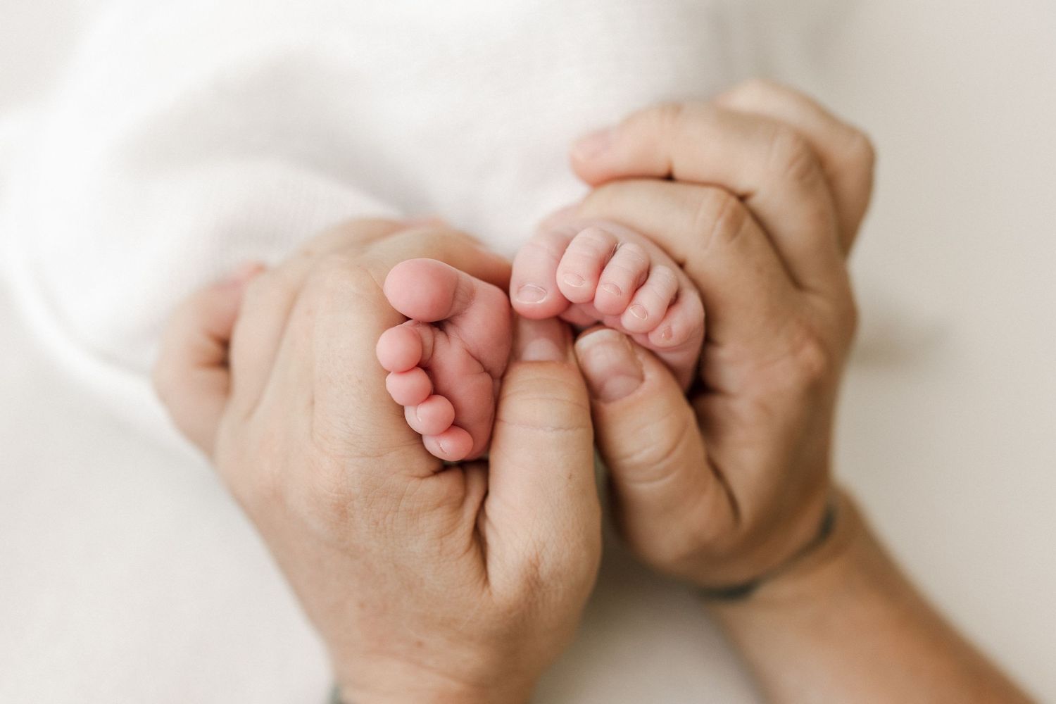 Adult hands gently cradling tiny baby feet against white background.