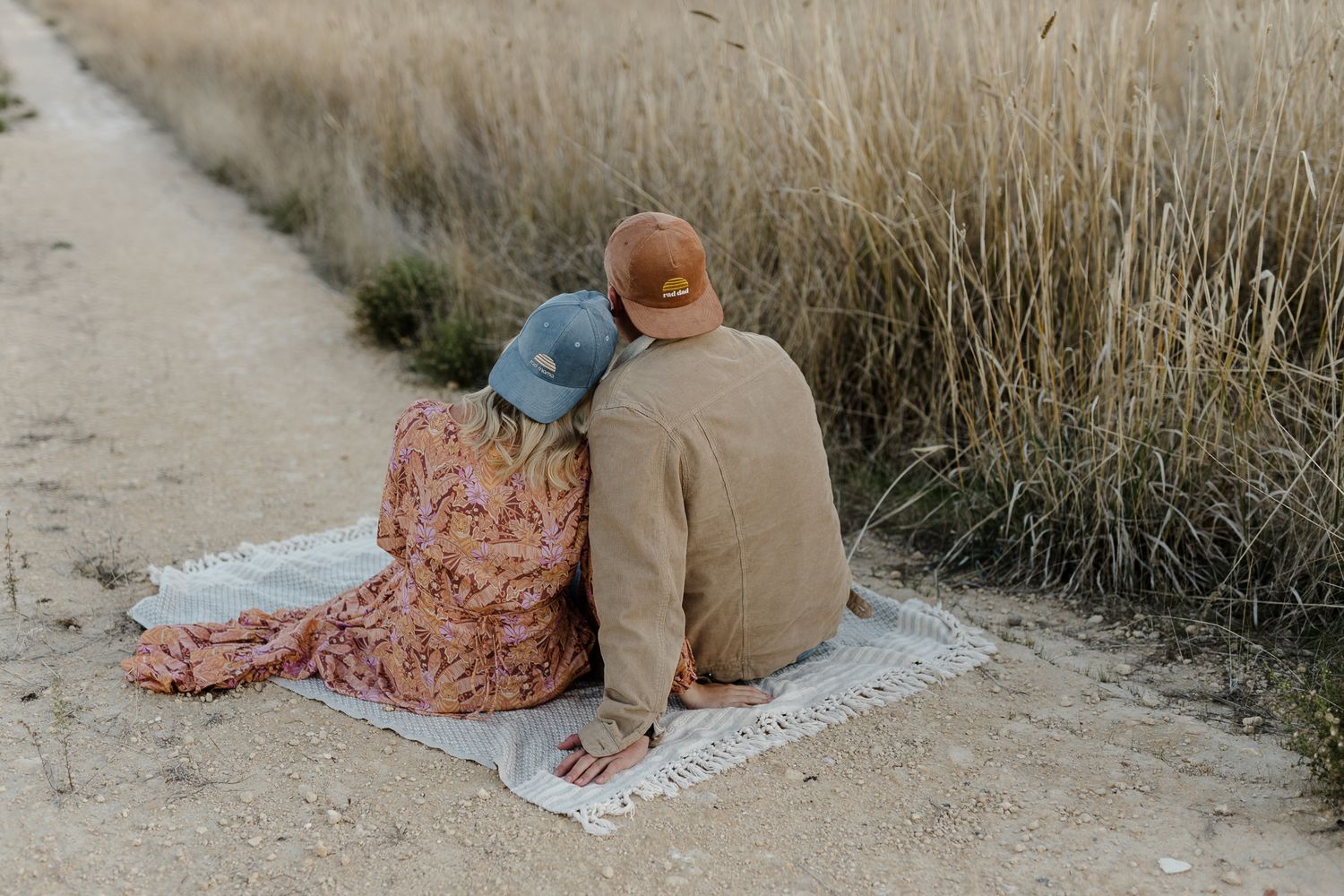 A couple sits together on a blanket along a nature trail bordered by golden grass.