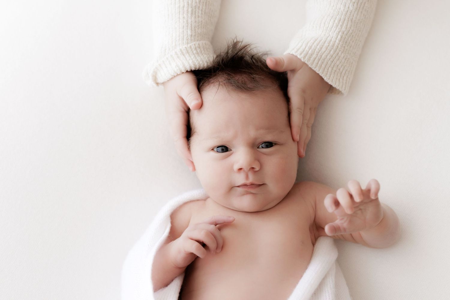 Baby lying on white surface with hands reaching overhead.