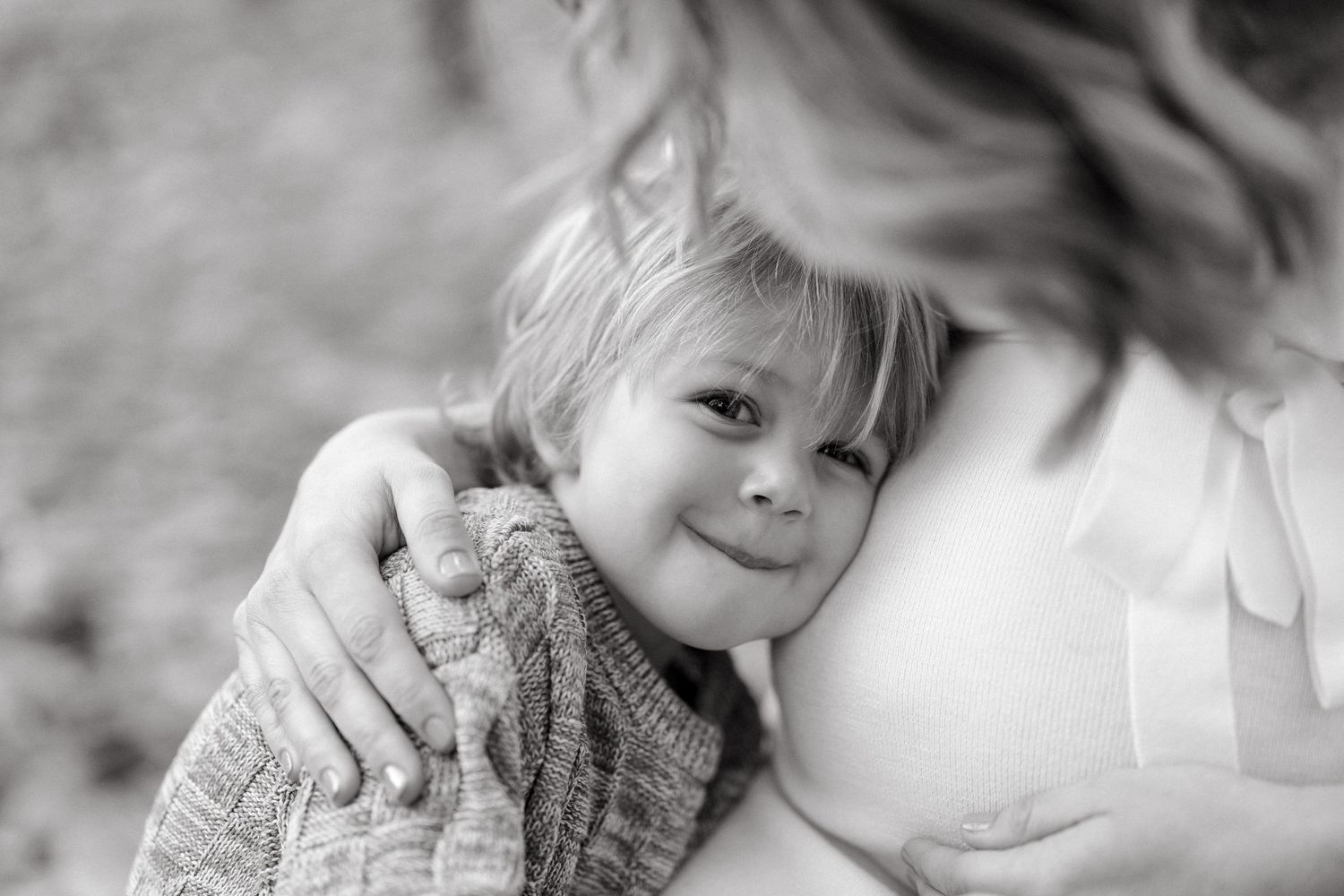 A black and white intimate portrait of a child in a knit sweater with their expectant mother.