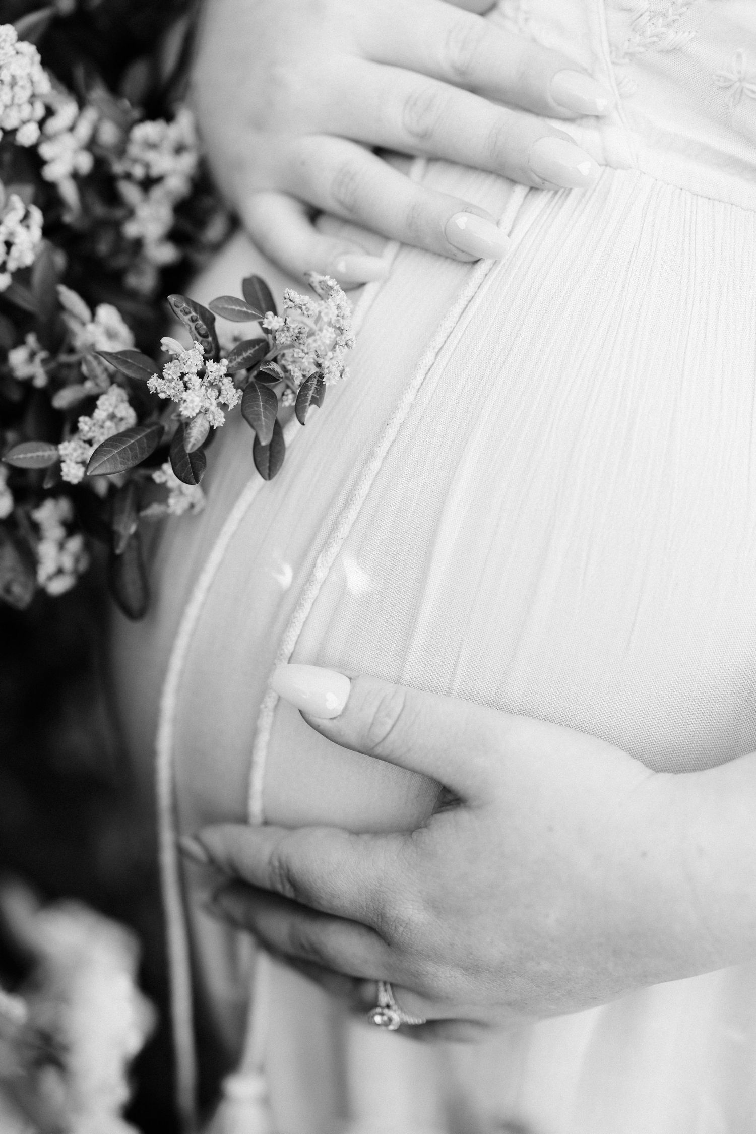 Close-up of hands cradling a pregnant belly with delicate white lace and small flowers.