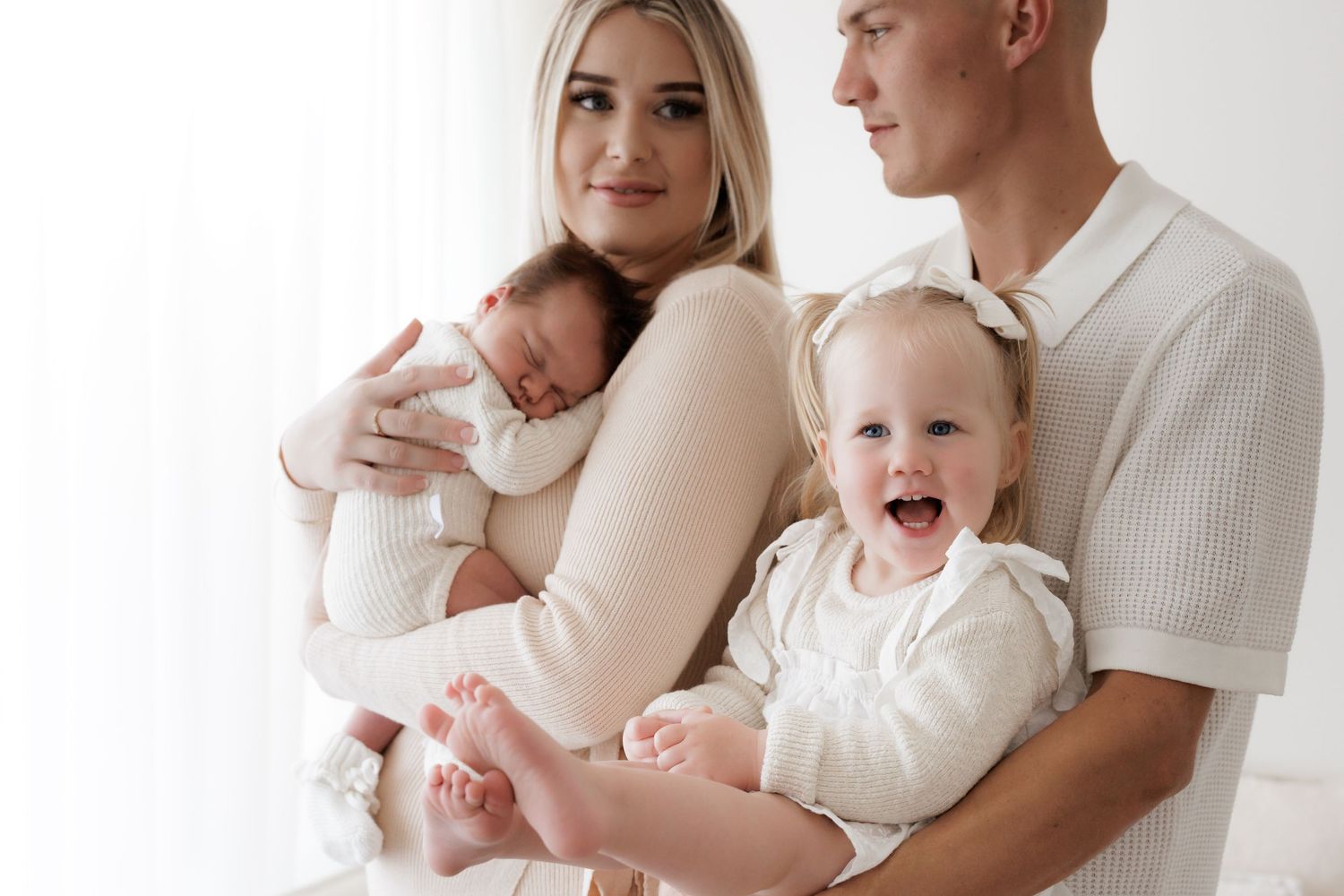 Family portrait with infant and toddler wearing matching cream outfits.