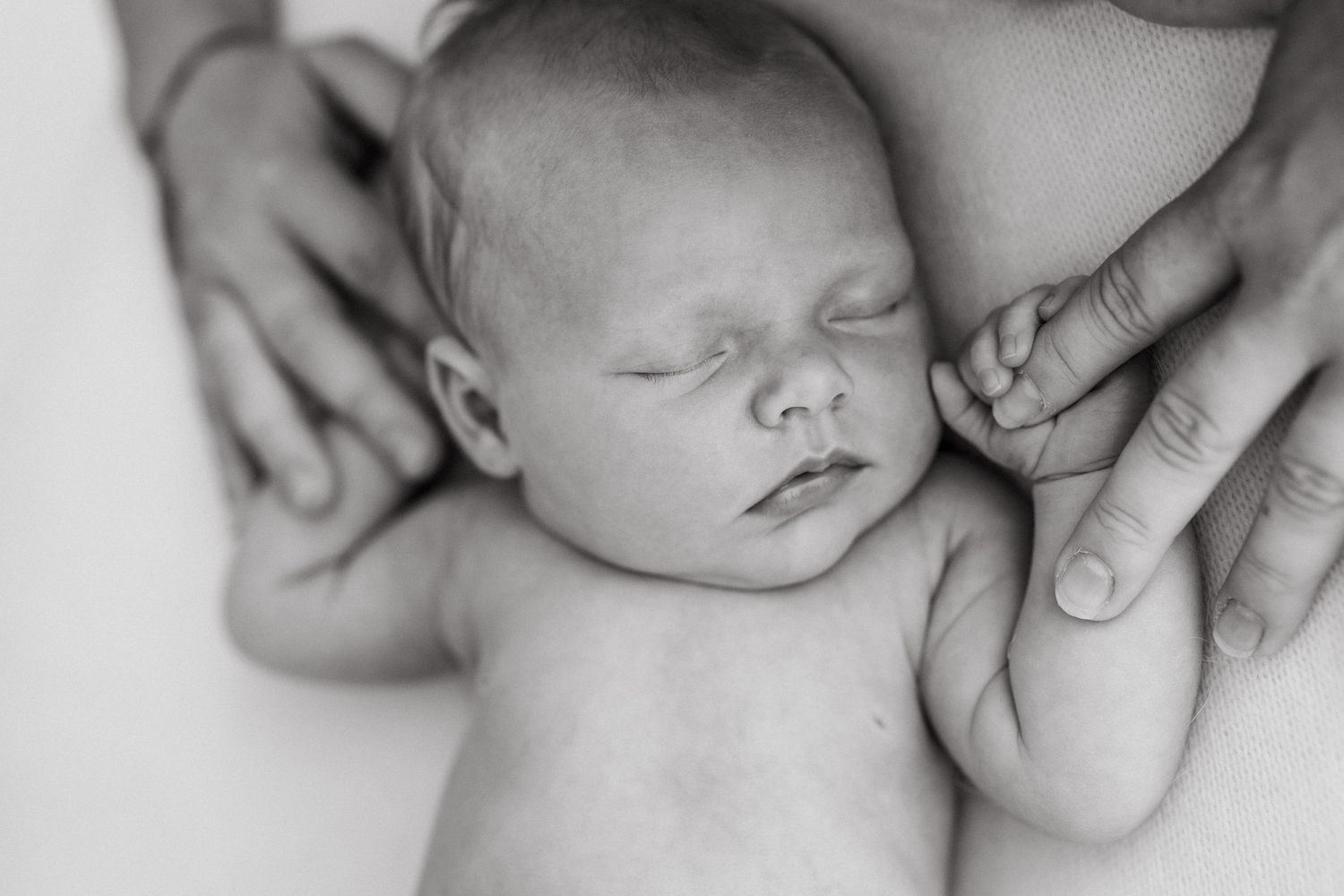 Peaceful newborn sleeping while hands provide gentle touch in black and white.