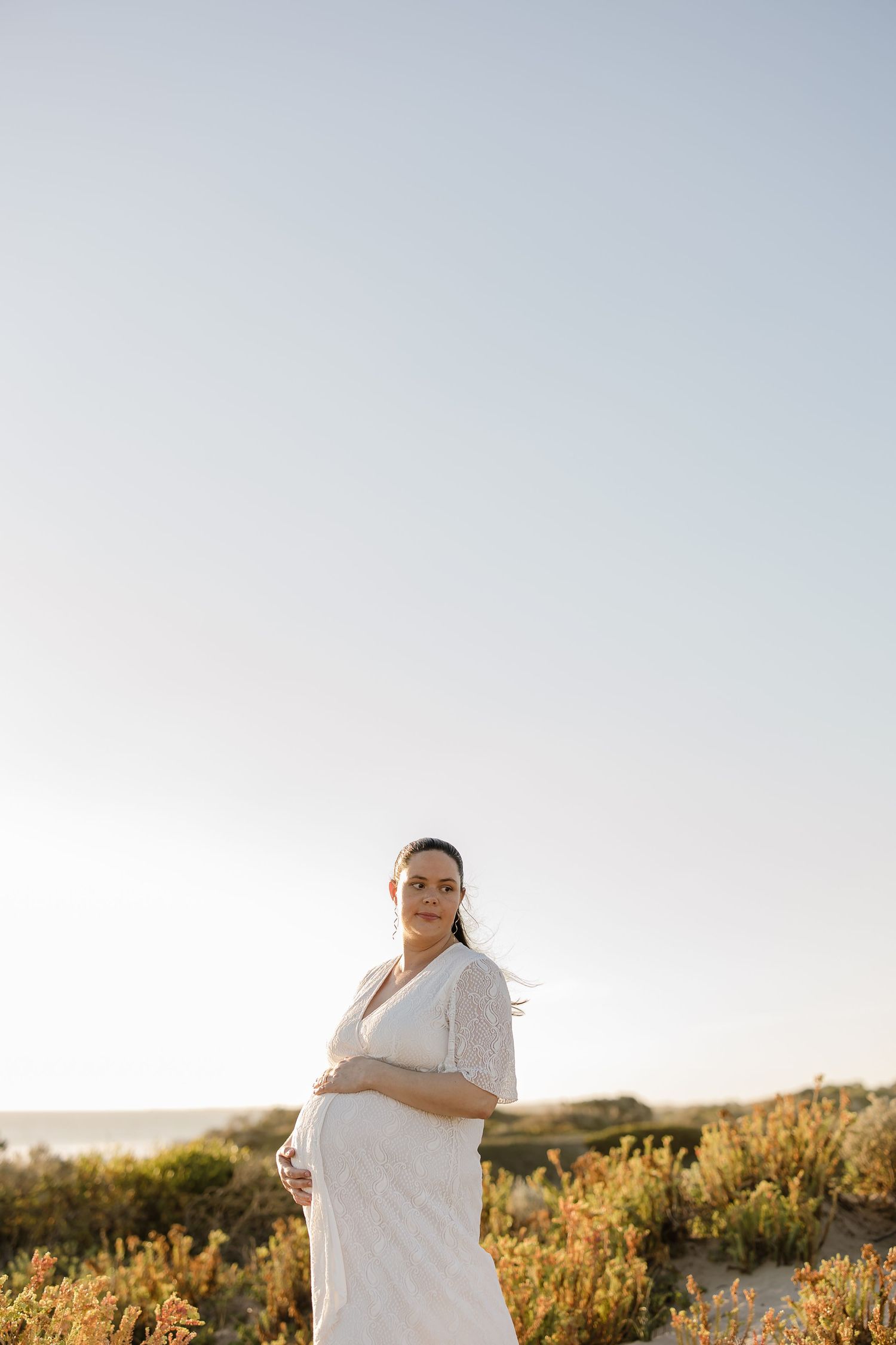 Woman in white dress standing in golden beach grass during sunset.