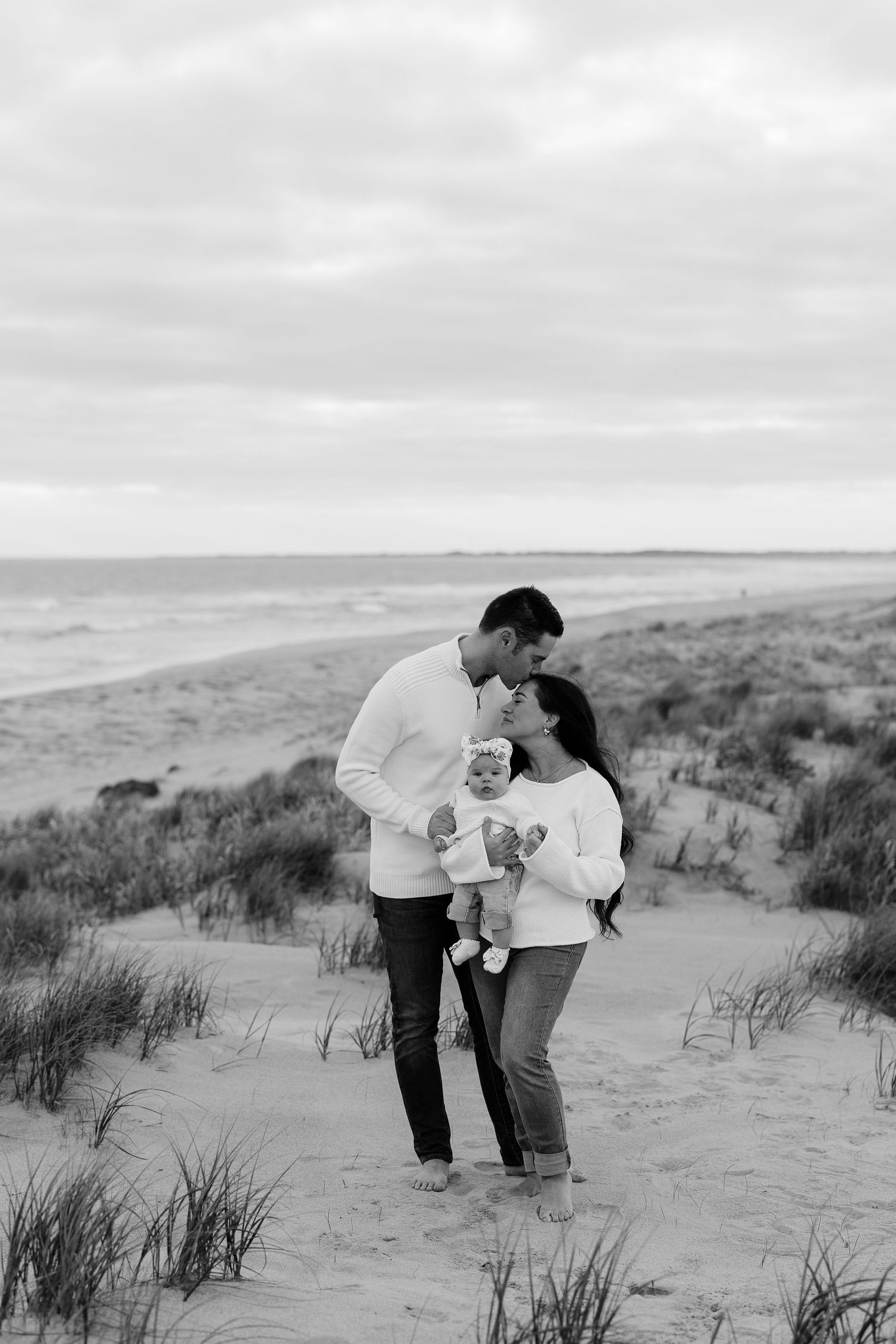 Intimate family moment captured on sandy dunes in black and white.