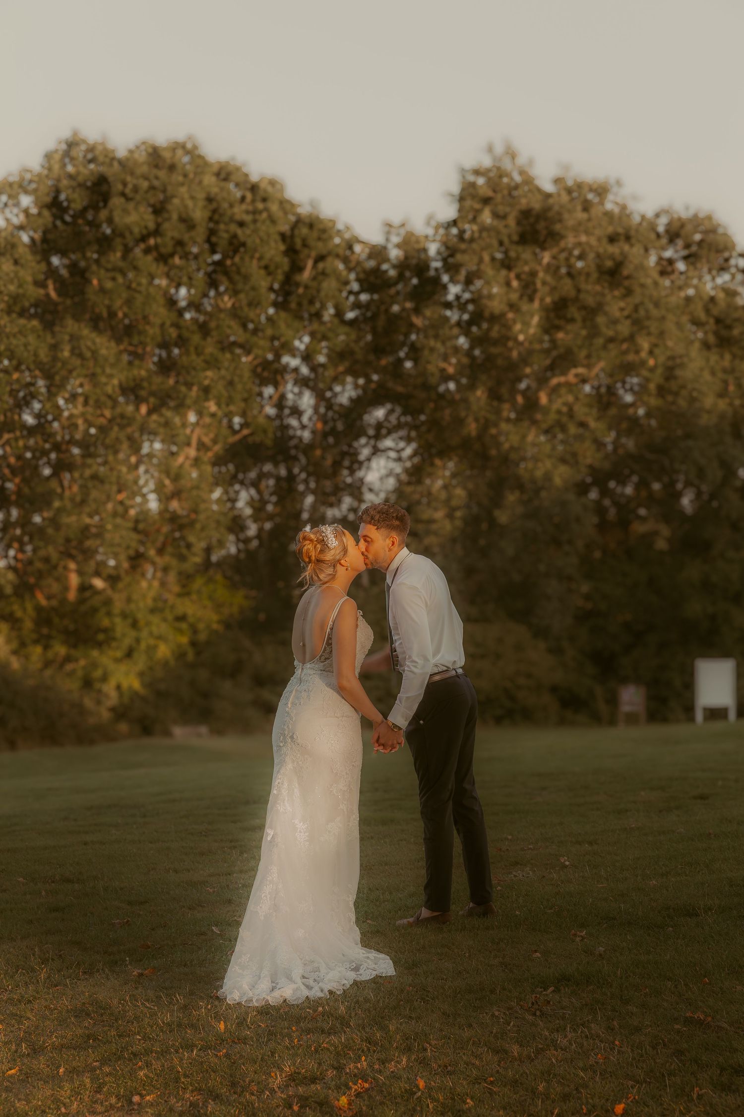 Golden hour wedding portraits in a scenic field with autumn trees in background.