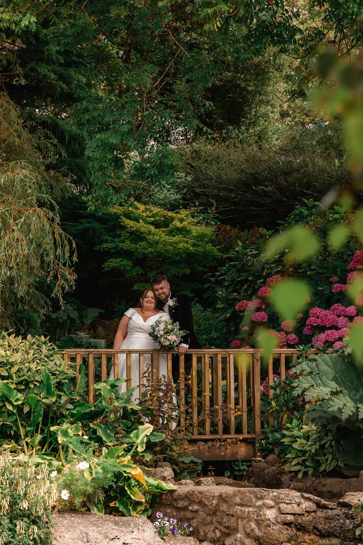 A couple sharing an intimate moment on a rustic wooden bridge in a lush garden setting.