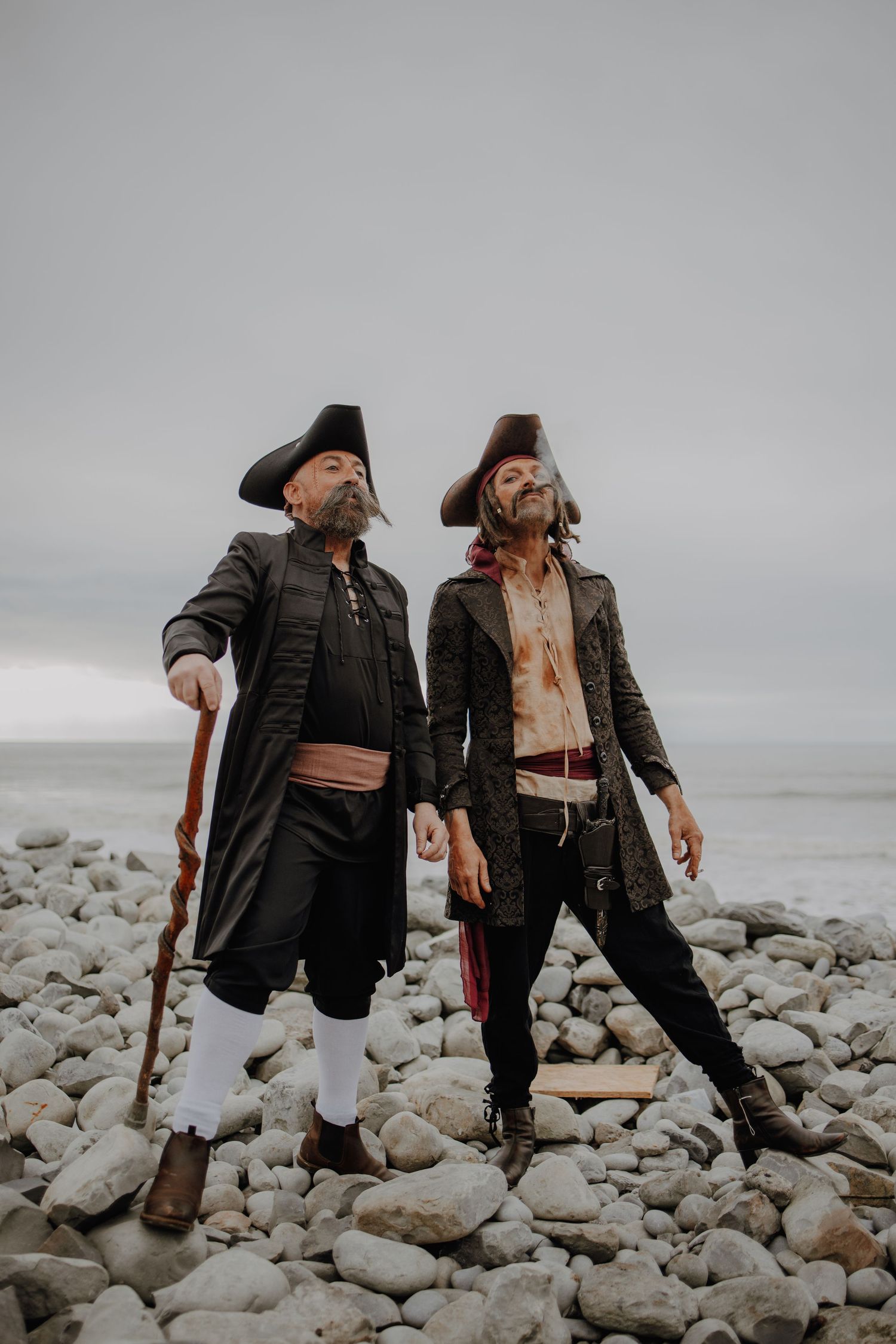 Two figures in pirate costumes posing dramatically on a rocky beach.
